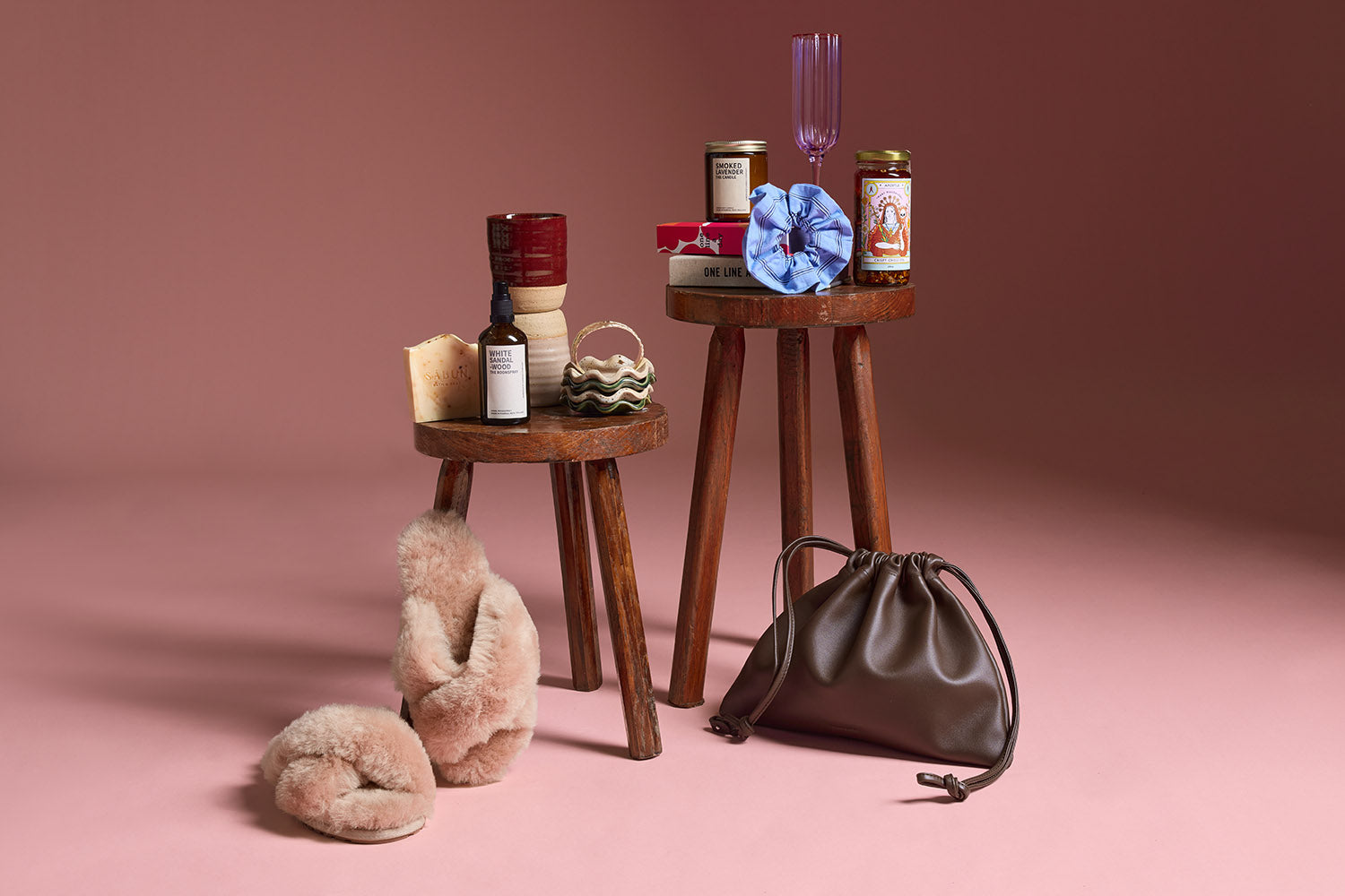 A collection of gifts on a blue background, including handbags, a straw hat, sunglasses, mugs, beauty products, a striped shirt, flowers, a candle, playing cards, and a book.