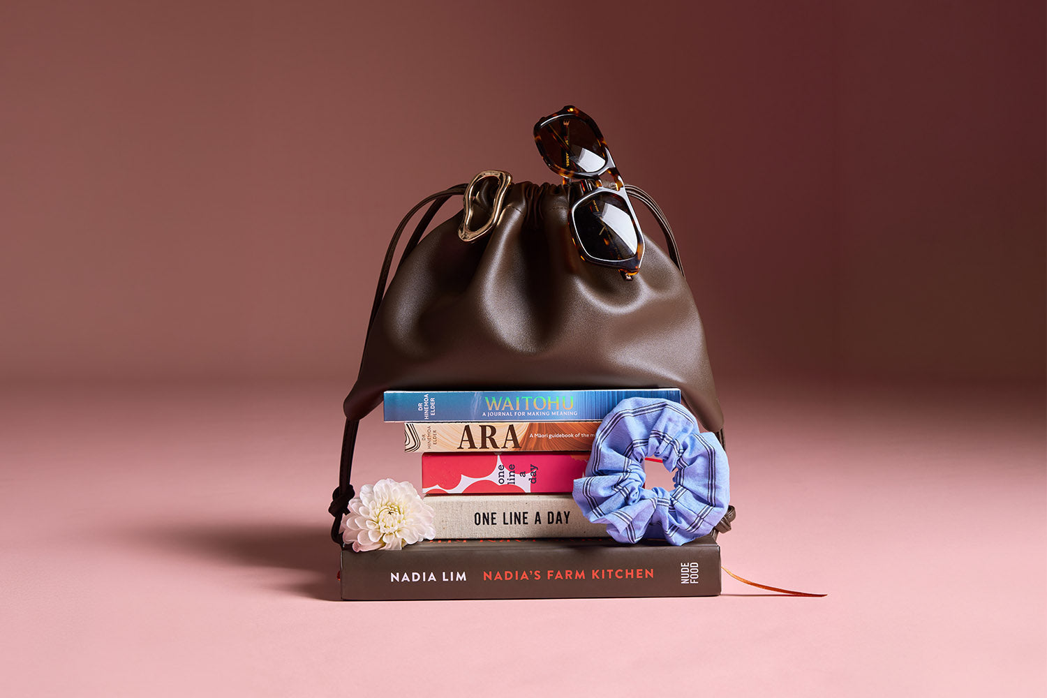 A stack of seven books and three heirloom tomatoes are arranged against a light blue background. Some books include titles like Find Your Calm and Nadias Farm Kitchen.