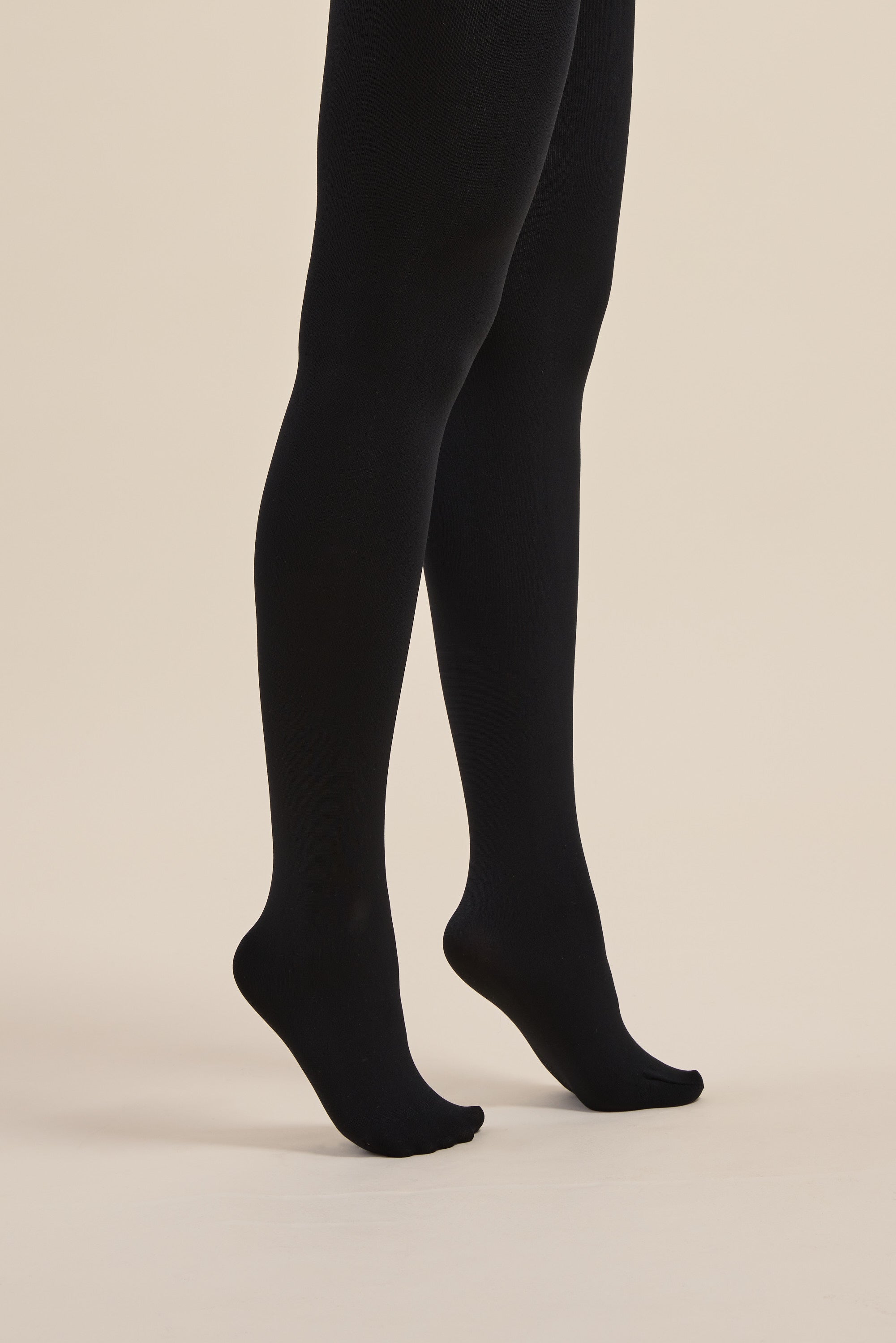 Person on tiptoes in Max Recycled Fleecy Tights, warm and opaque, against a beige background.