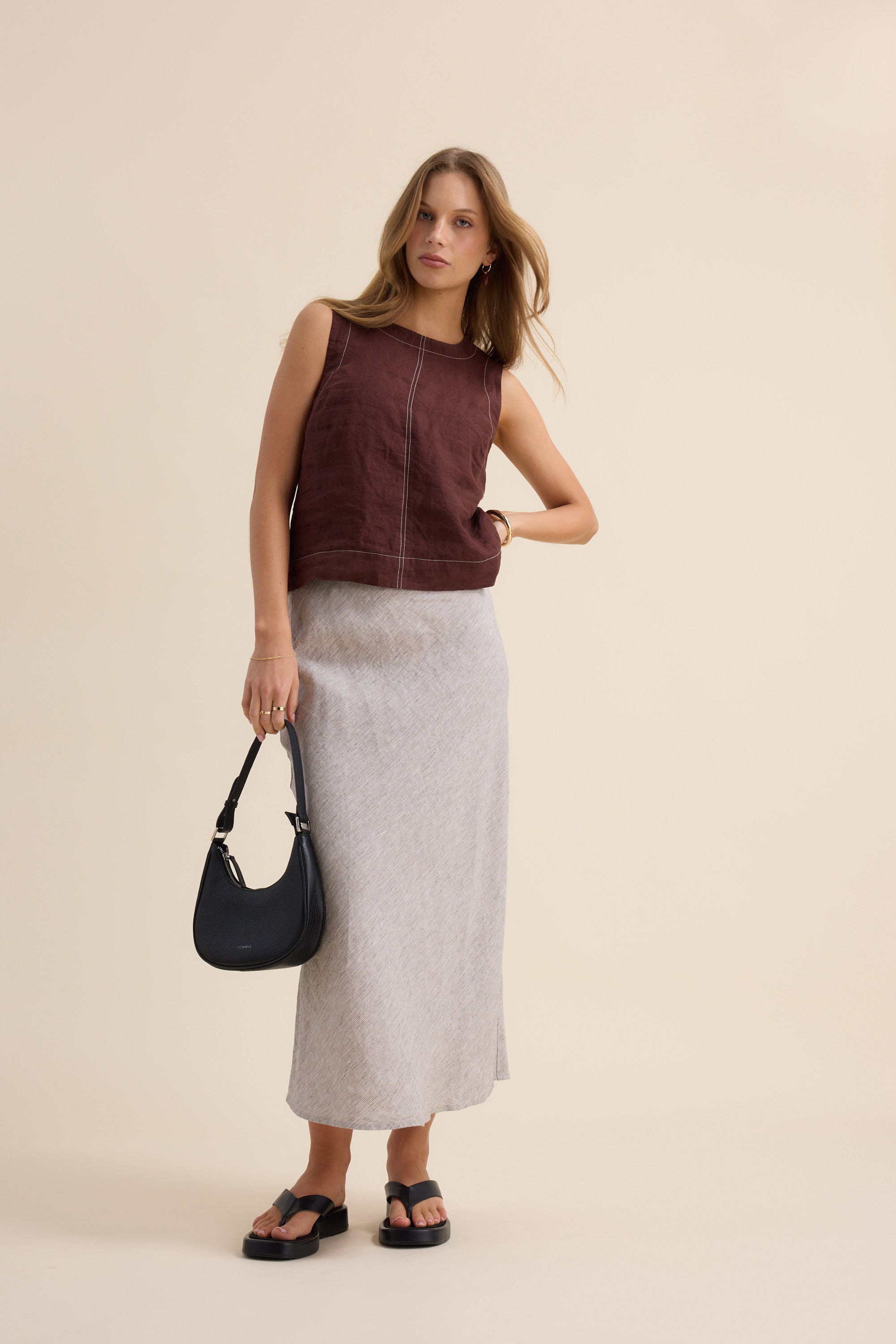 Woman in sleeveless maroon top, Max The Linen Slip Skirt, holding black handbag.