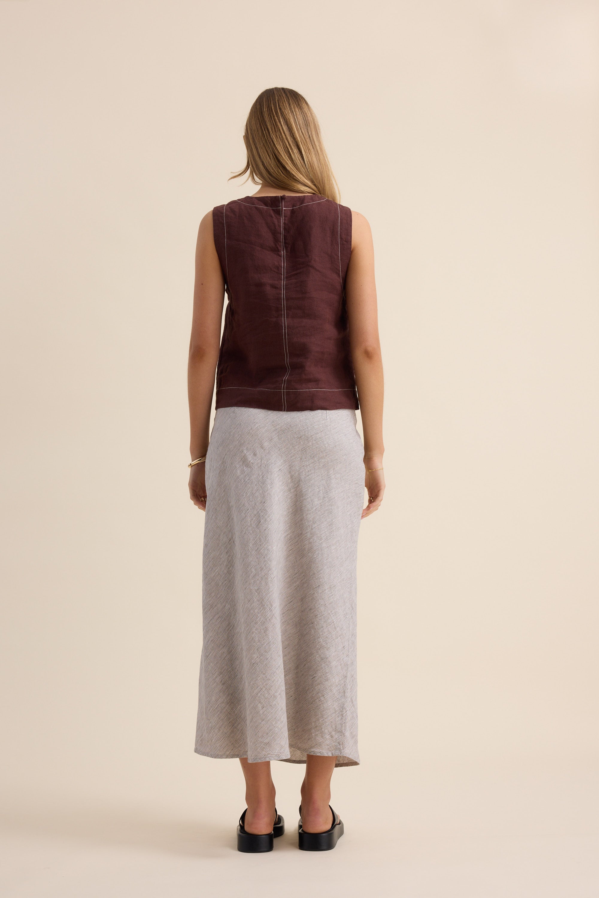 Woman in a sleeveless maroon top and Max The Linen Slip Skirt, facing away from camera.