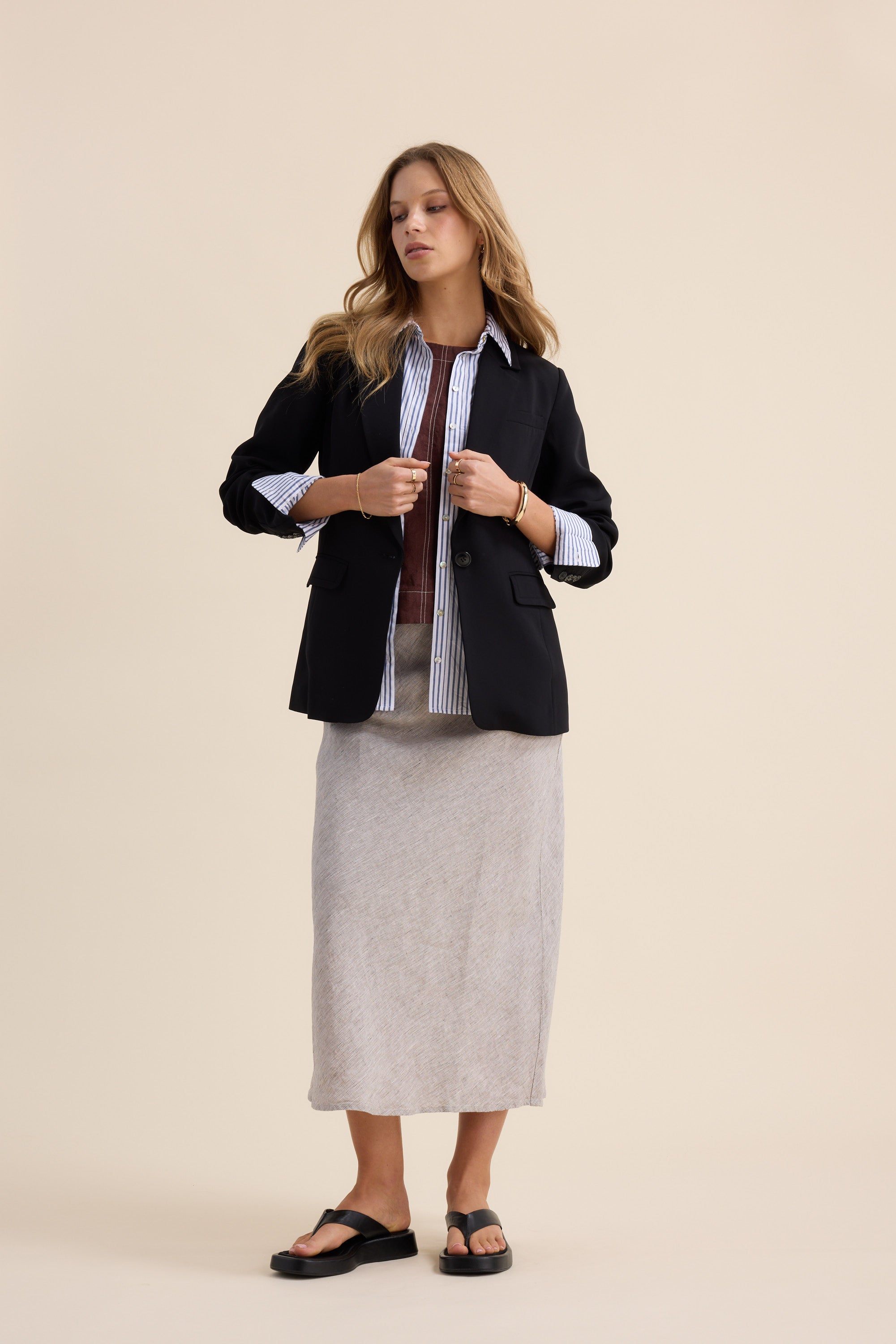 Woman in Max's Linen Slip Skirt, black blazer, and striped shirt against beige background.