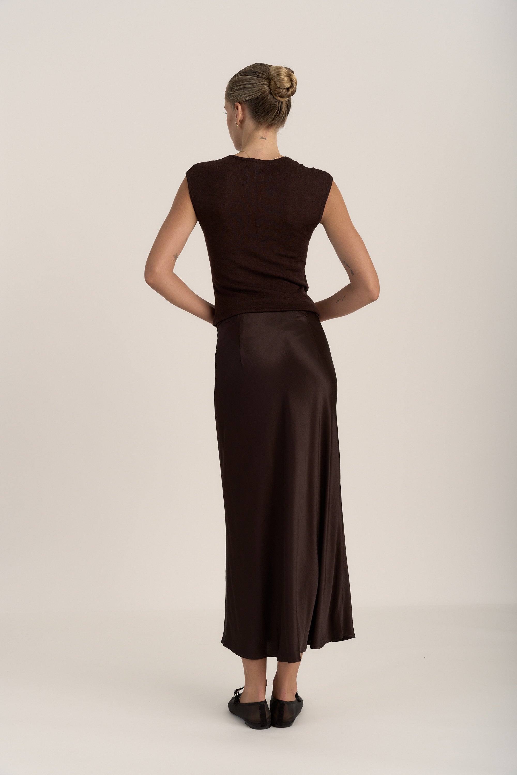 Woman in a dark top and Max The Slip Skirt stands facing away, hair styled in a bun.