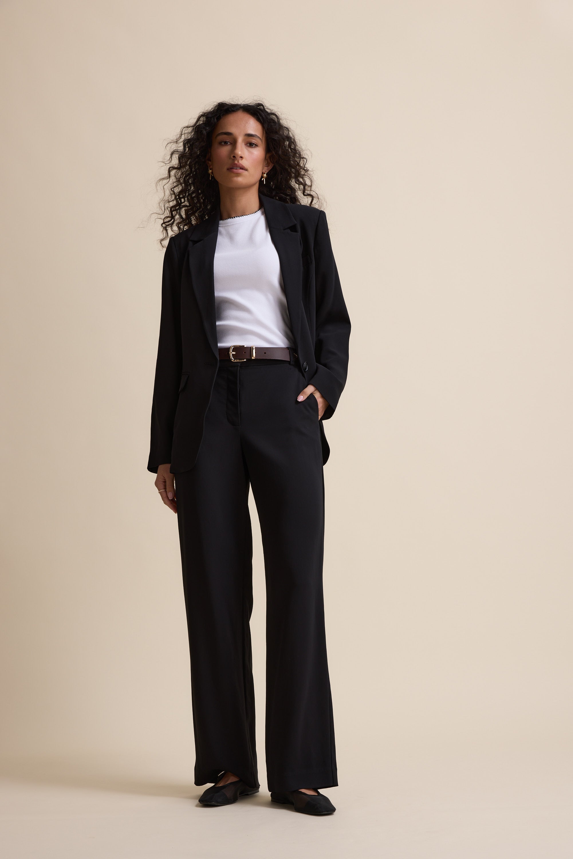 Woman in Max's The Wide Leg Pants and white top stands against a beige background, facing forward.