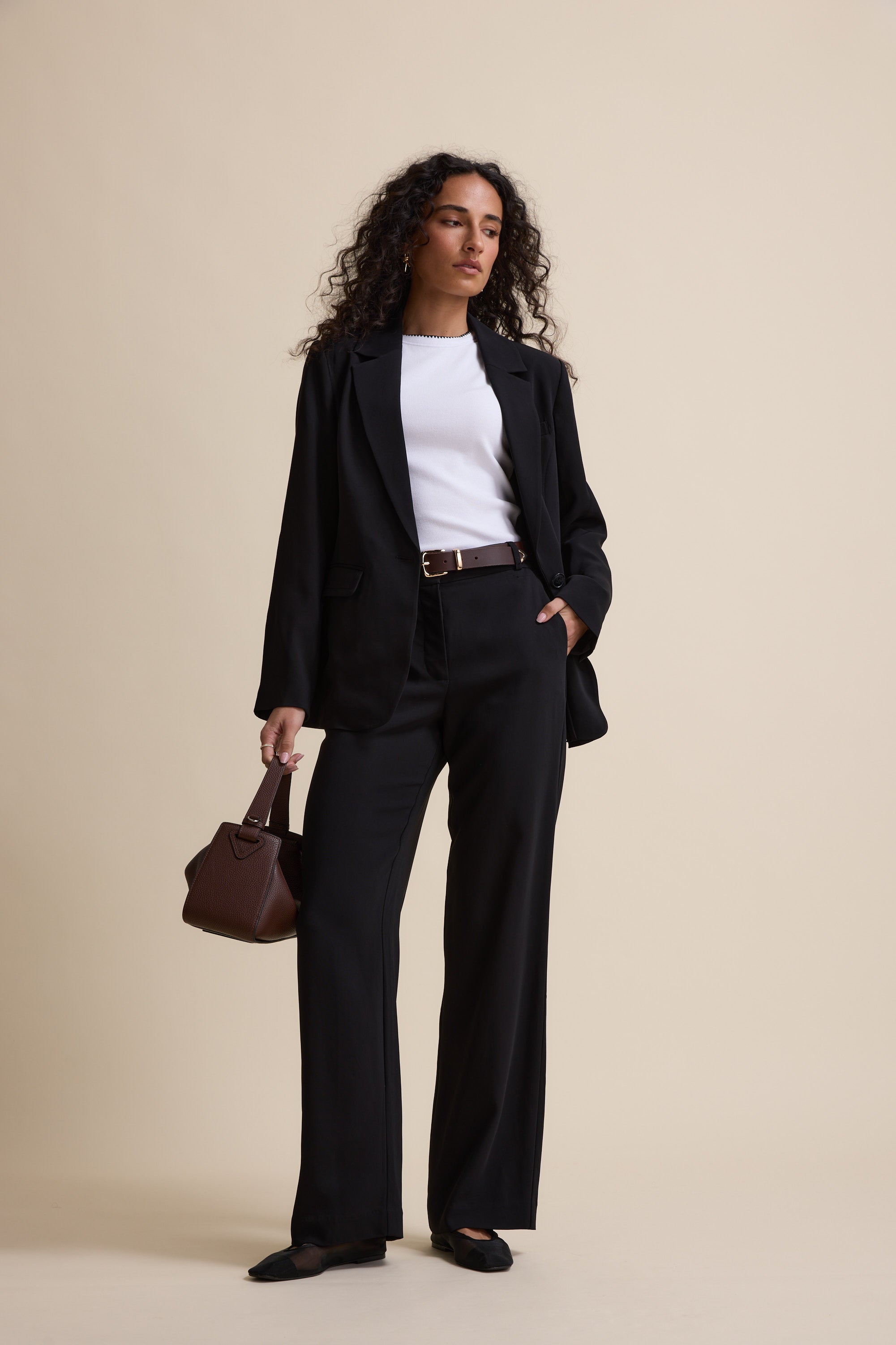 Woman in Max’s The Wide Leg Pants, black suit, holding a brown handbag.