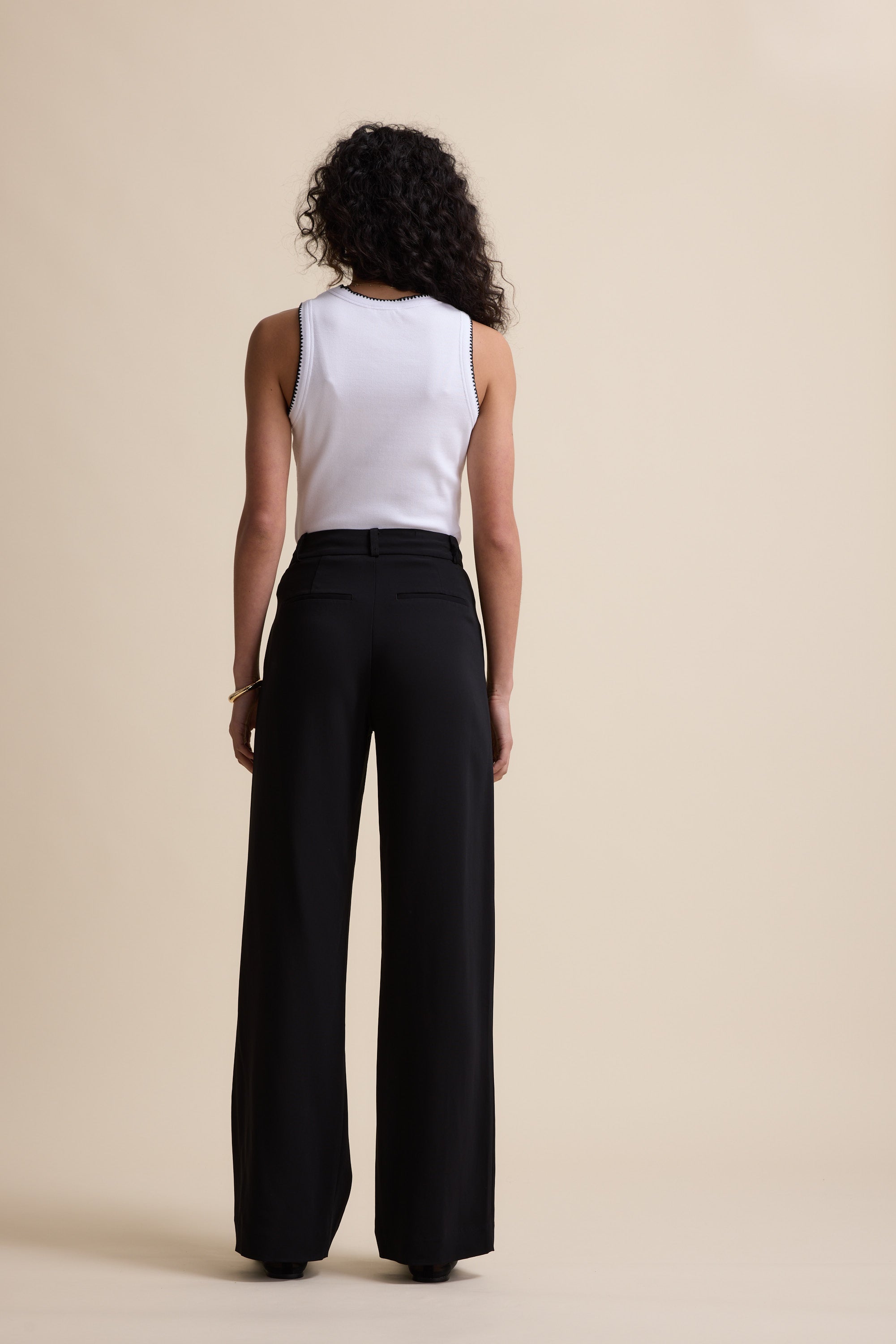 Person with curly hair in a white sleeveless top and Max's The Wide Leg Pants, facing away.