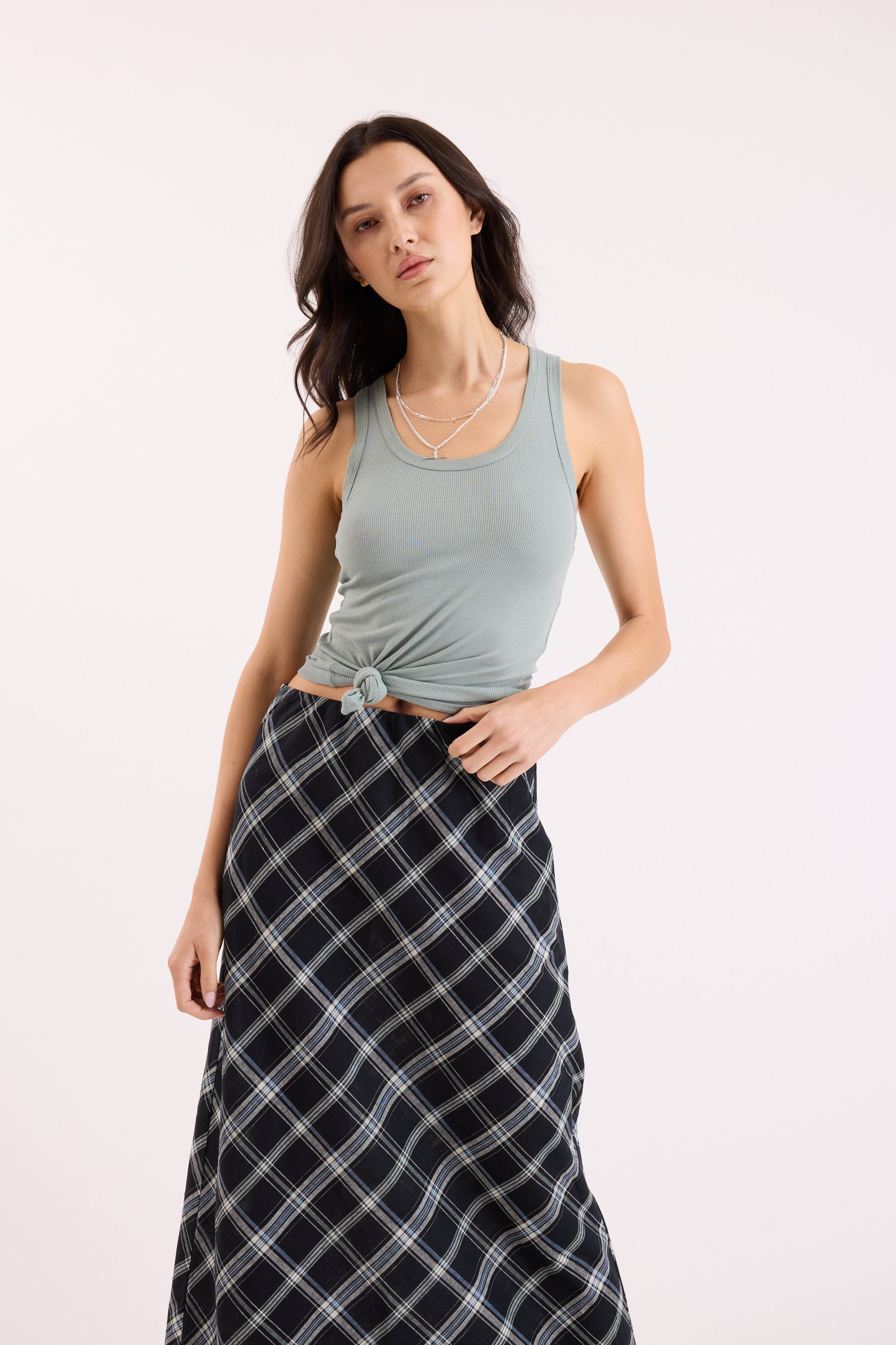 Woman wearing Max Sienna Ribbed Tank and plaid skirt, posing against a plain background.