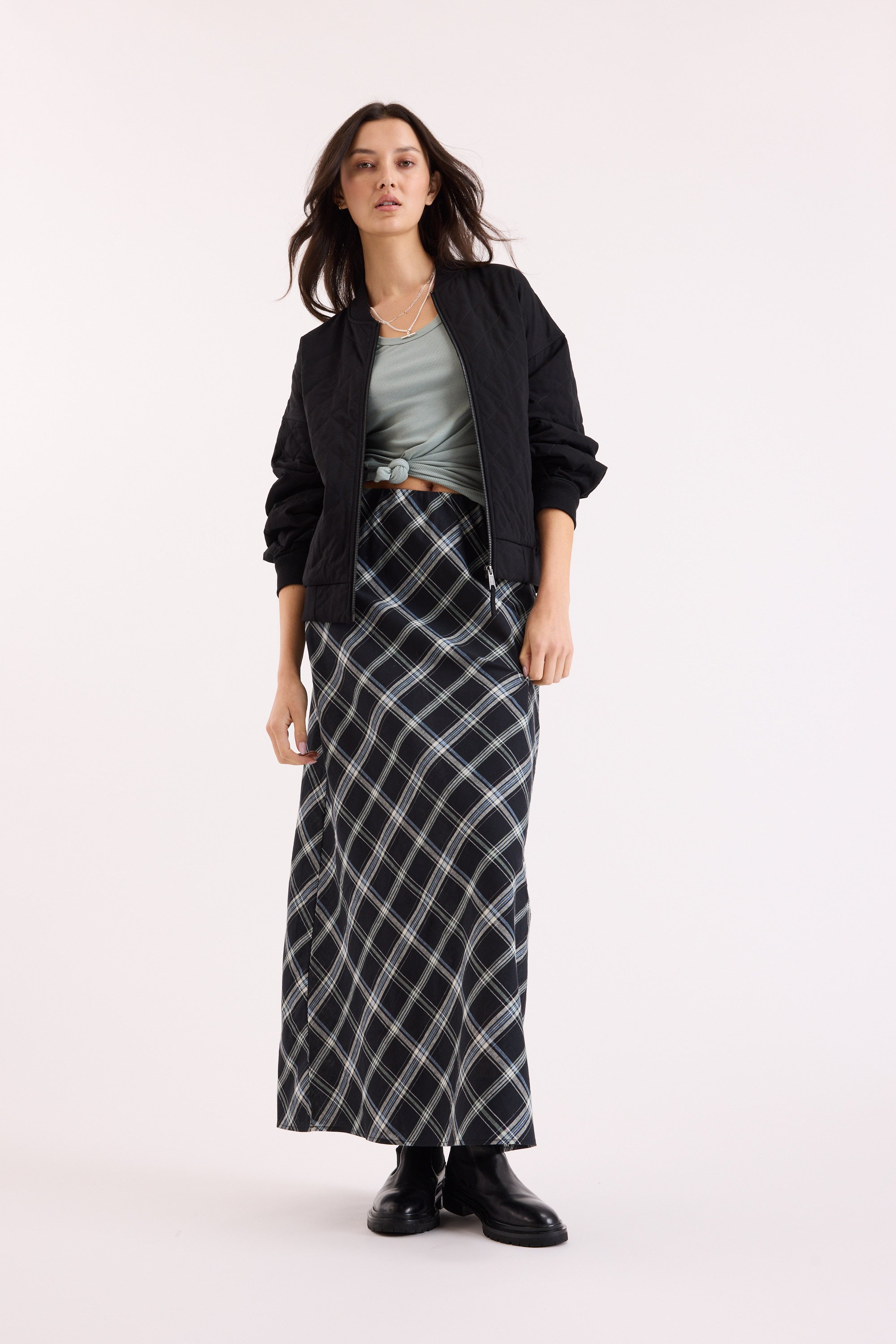 Woman in a black jacket, Max Sienna Ribbed Tank, plaid maxi skirt, and black boots.