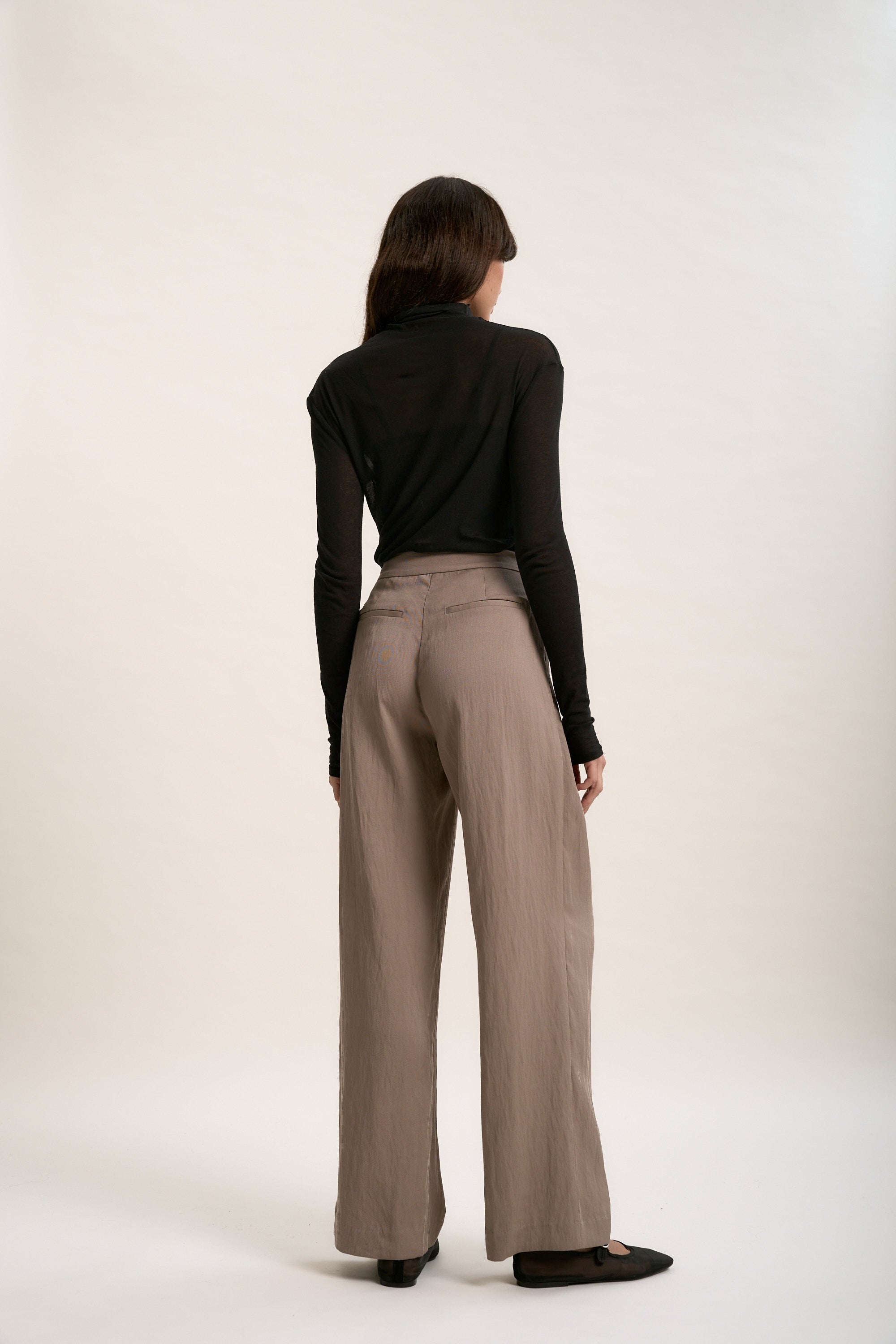 Woman in Max's The Ultimate Wide Leg Pants and black top, facing away against plain background.