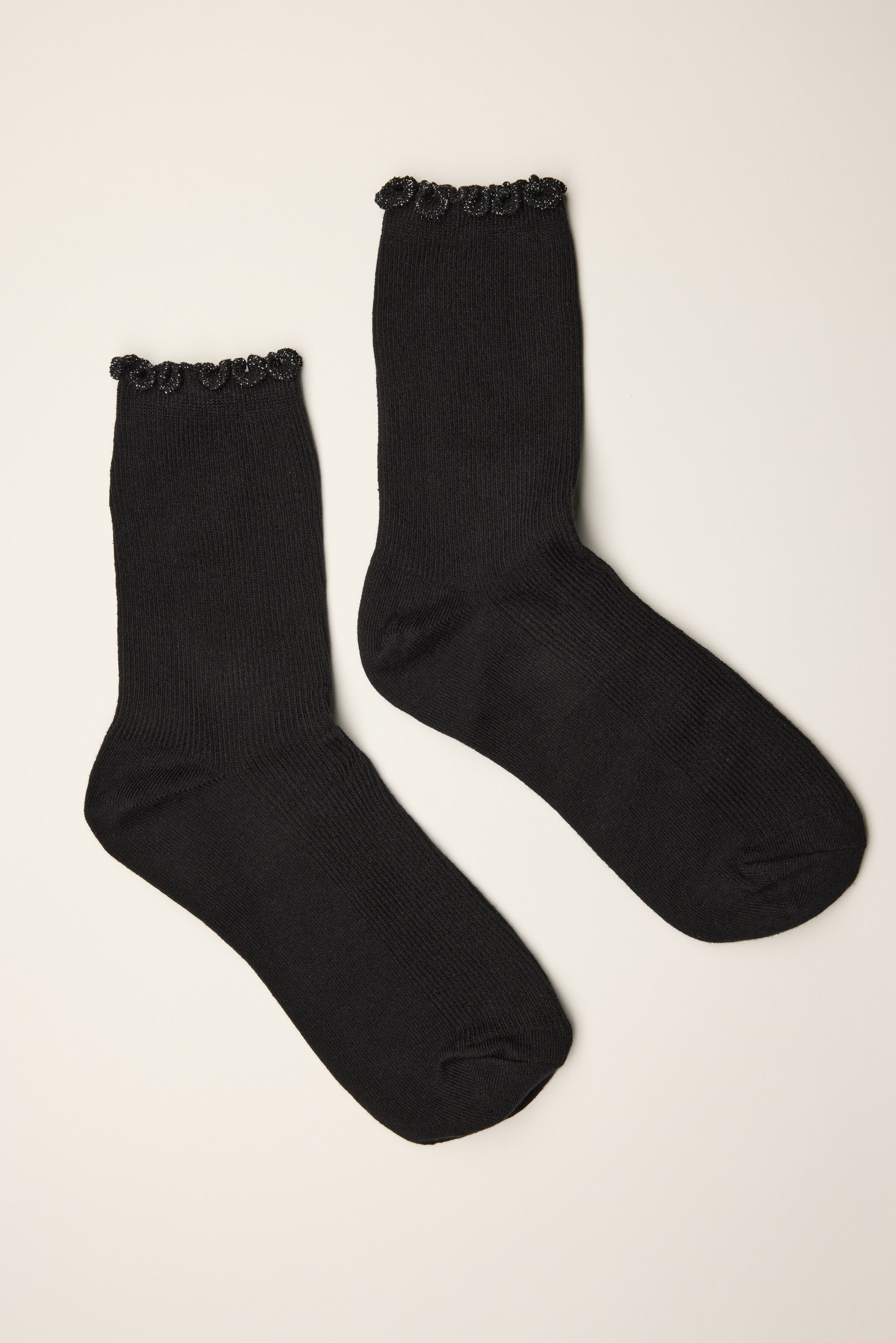A pair of Max's Sophia Lurex Ruffle Top Crew Socks in black, featuring a scalloped lace trim at the top, is laid flat on a neutral background.