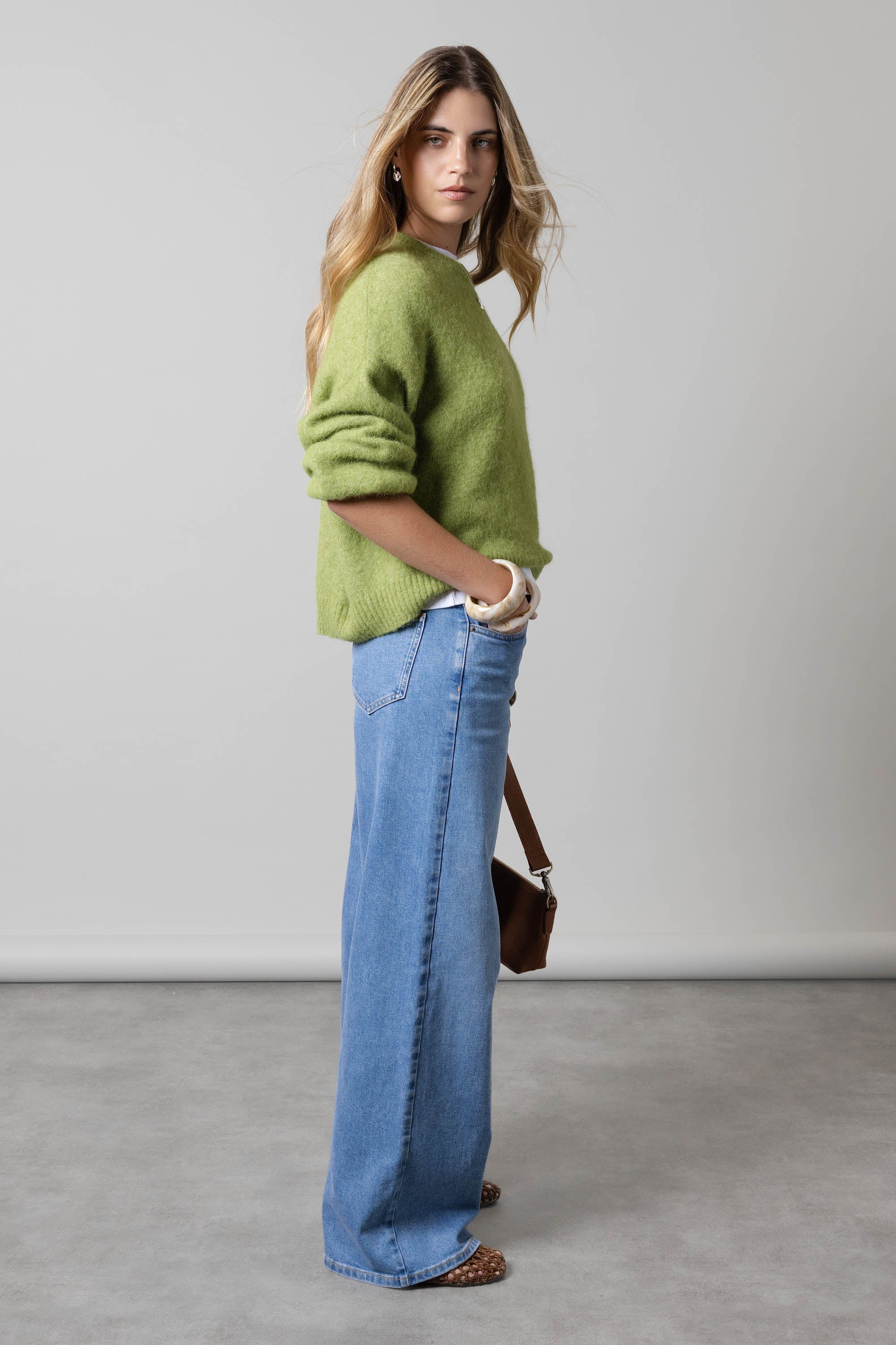 Woman in green sweater and Max Nevada Wide Jeans stands sideways against a plain background.