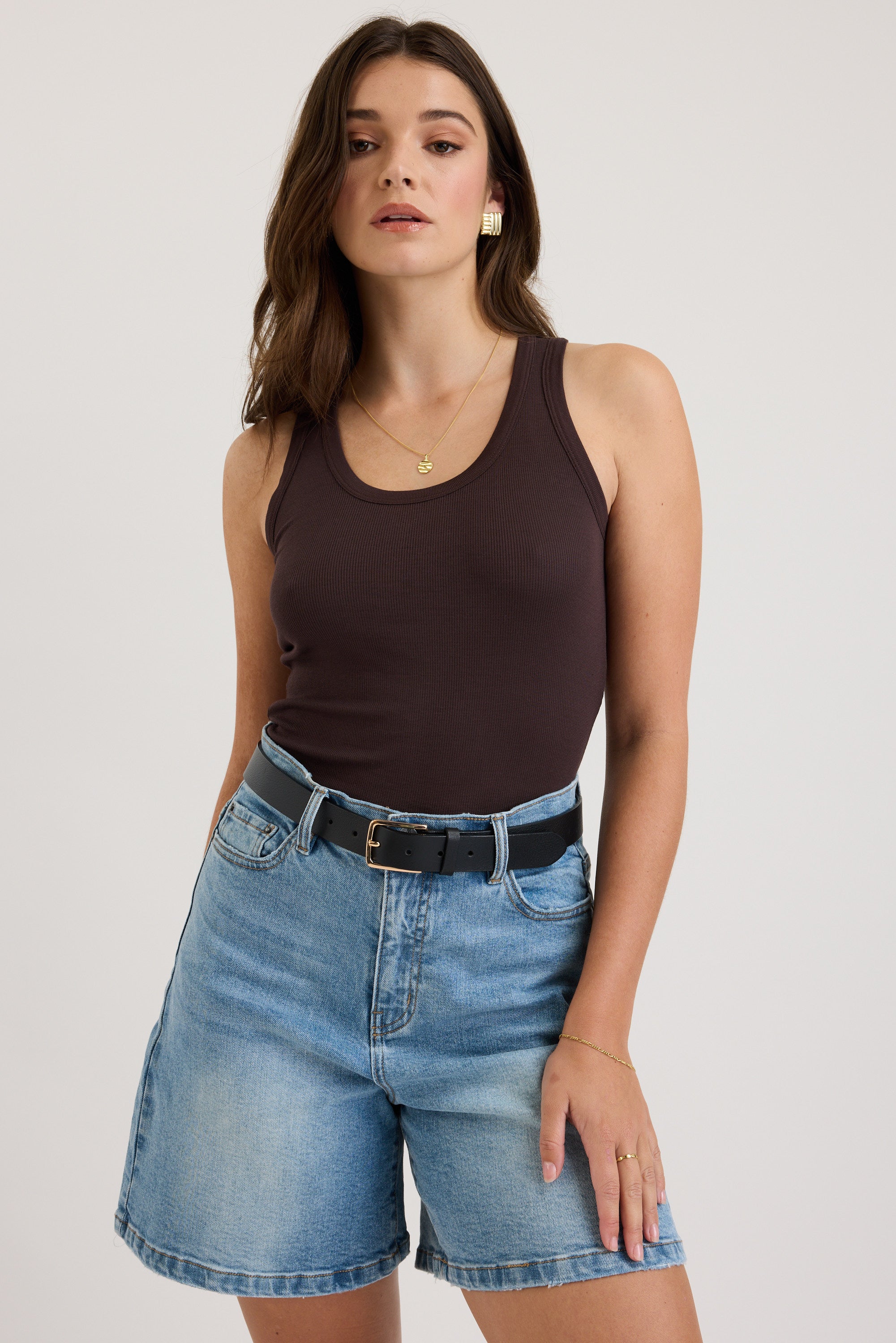 Woman wears Max's The Ultimate Denim Short and a brown tank top, hand in her pocket.