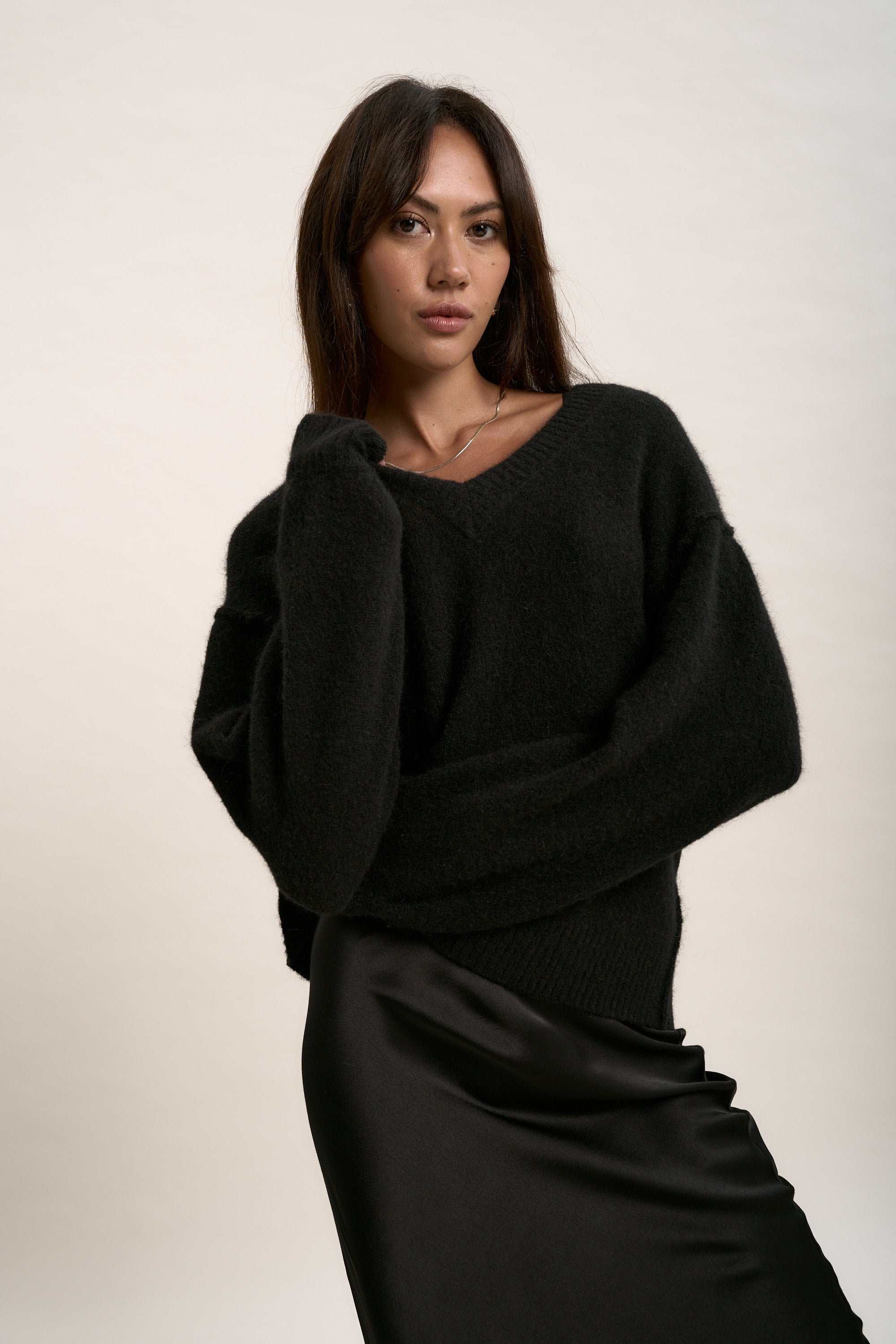 Woman wearing Max's Luxe Whisper V Neck Sweater with a black satin skirt, posing simply.