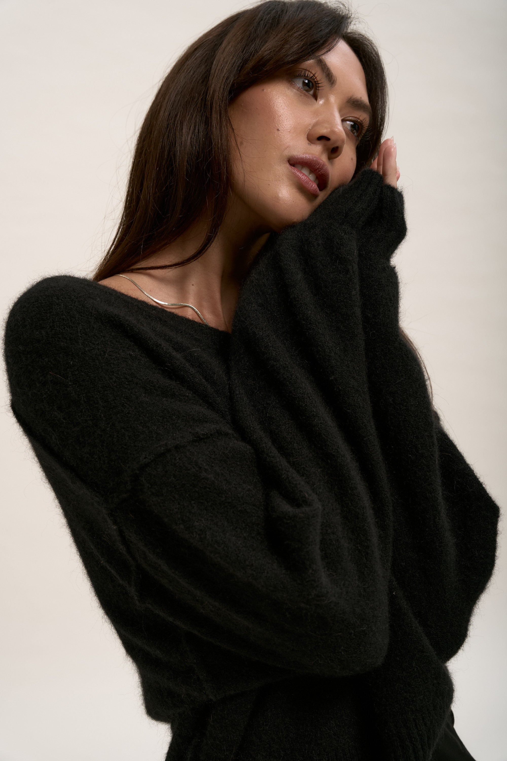 Woman in The Luxe Whisper V Neck Sweater by Max poses with hand on face, gazing upward.