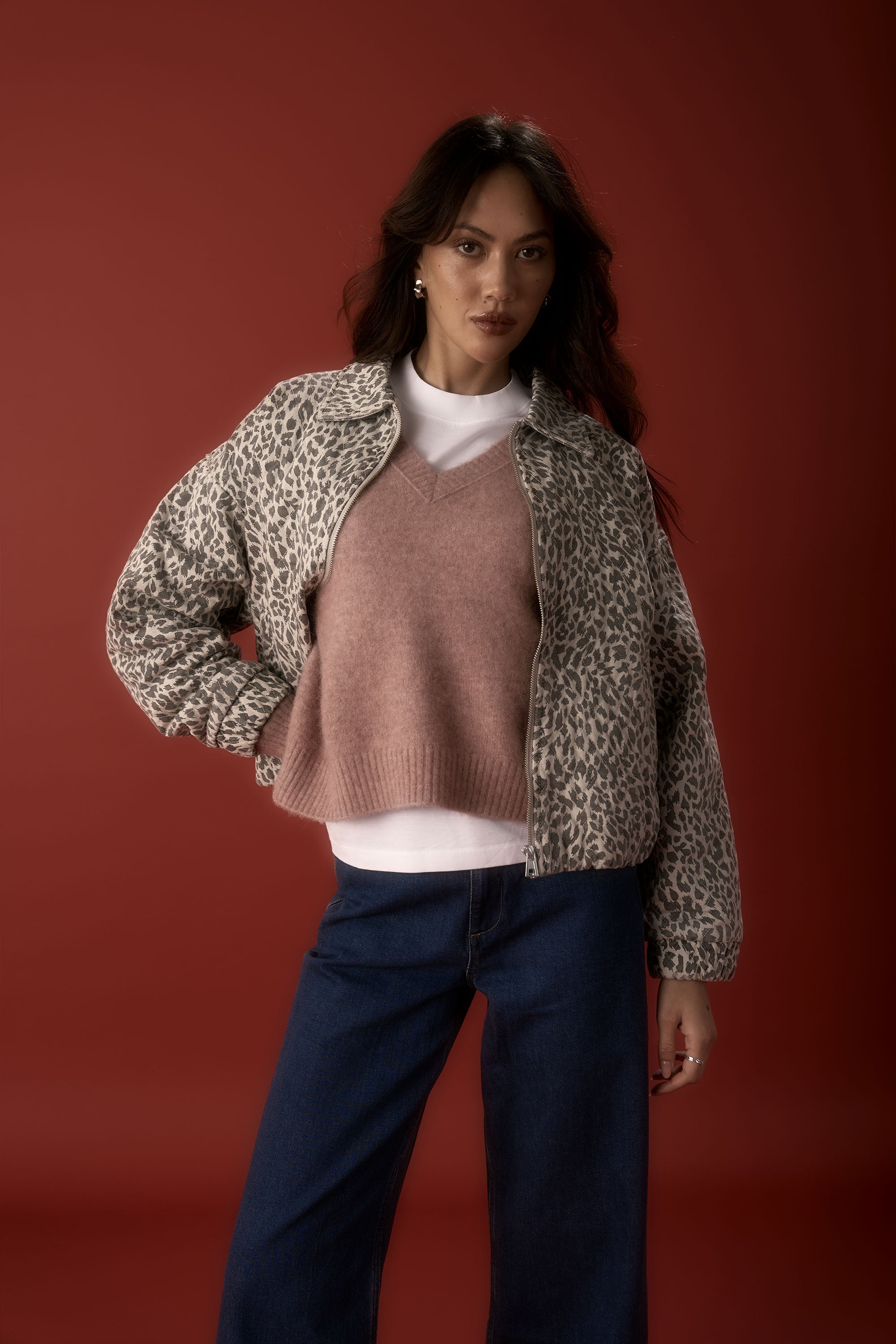 Woman in Max’s Luxe Whisper V Neck Sweater and leopard-print jacket poses by a red backdrop.