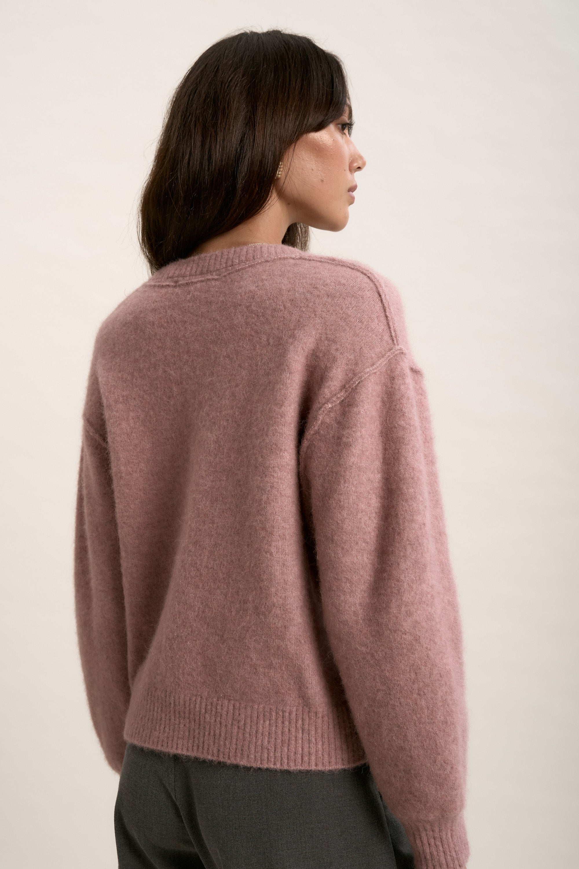 Woman with long brown hair in Max’s Luxe Whisper V Neck Sweater, pink and fuzzy, back view.