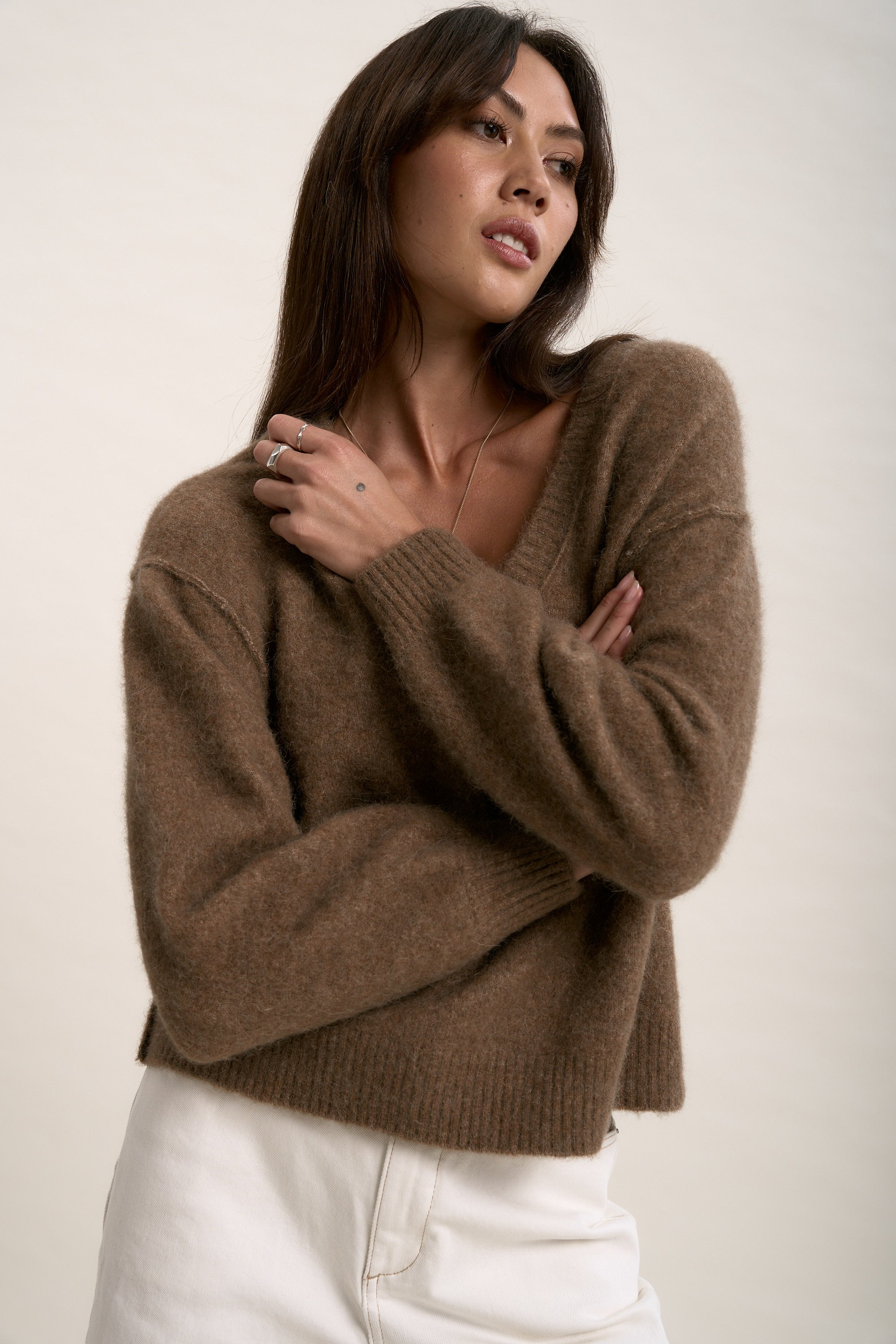 Woman in Max's Luxe Whisper V Neck Sweater and white pants poses stylishly with arms crossed.