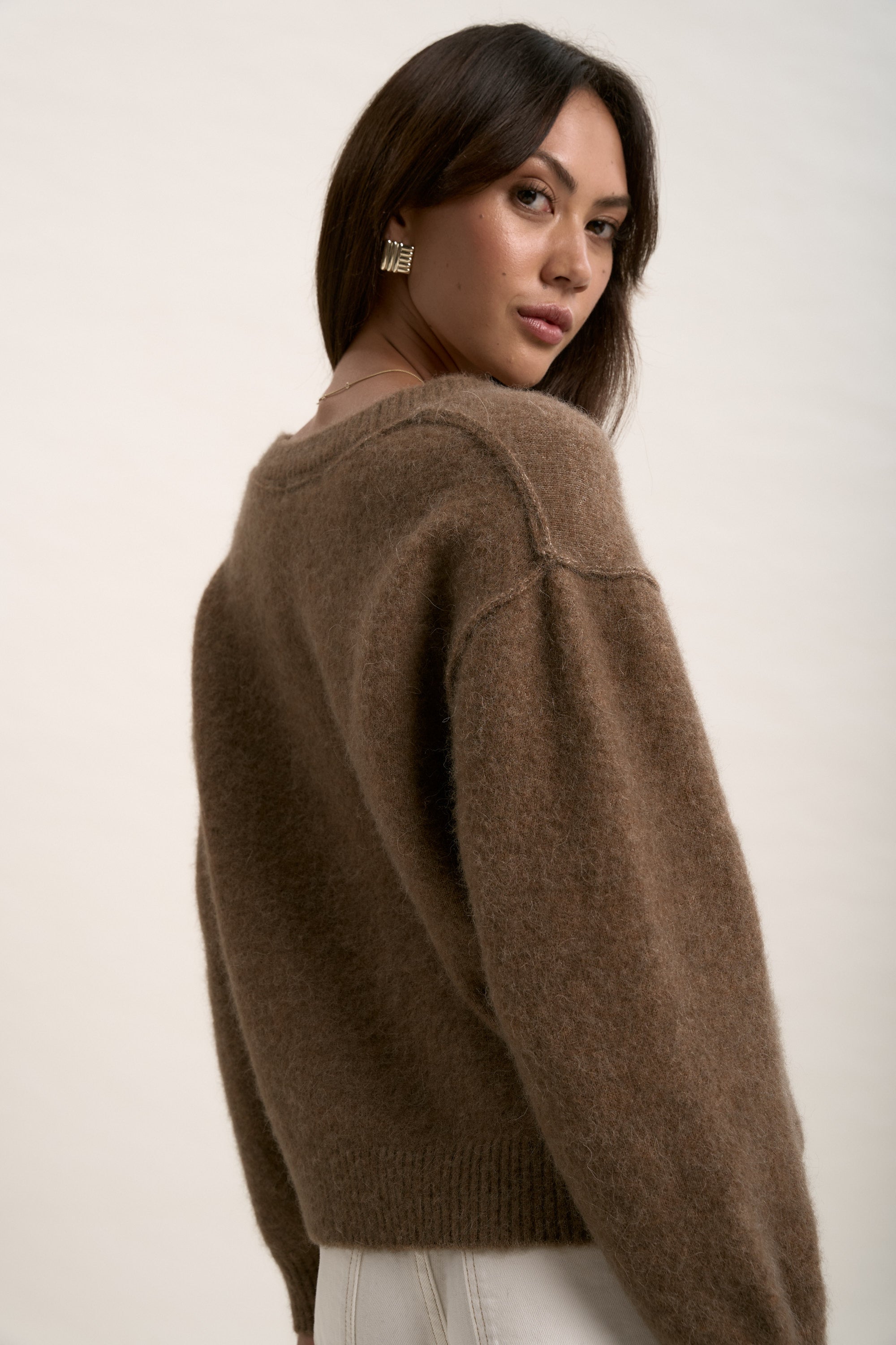Woman in The Luxe Whisper V Neck Sweater by Max looks over her shoulder against a plain backdrop.