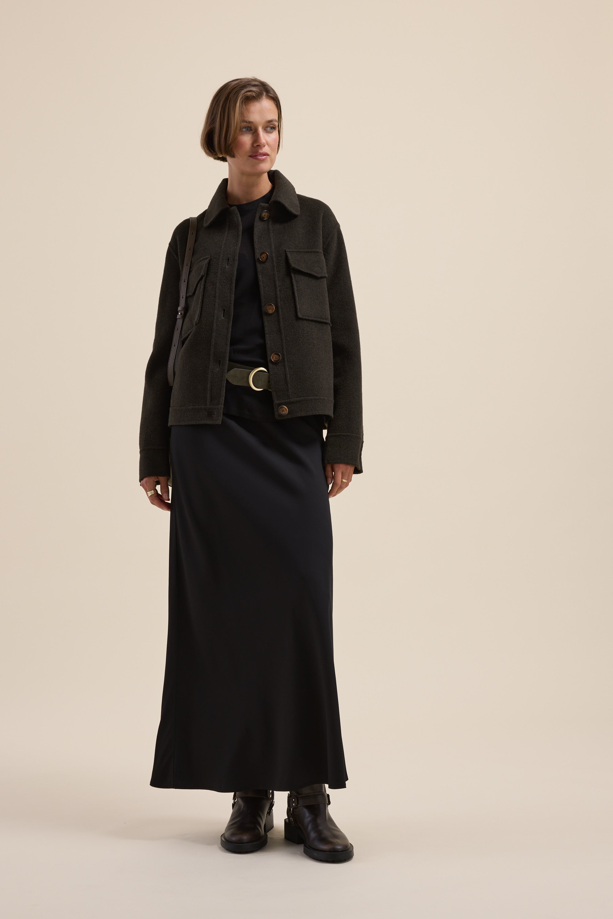 Woman in Max's The Maxi Slip Skirt and dark jacket with boots, against a beige background.