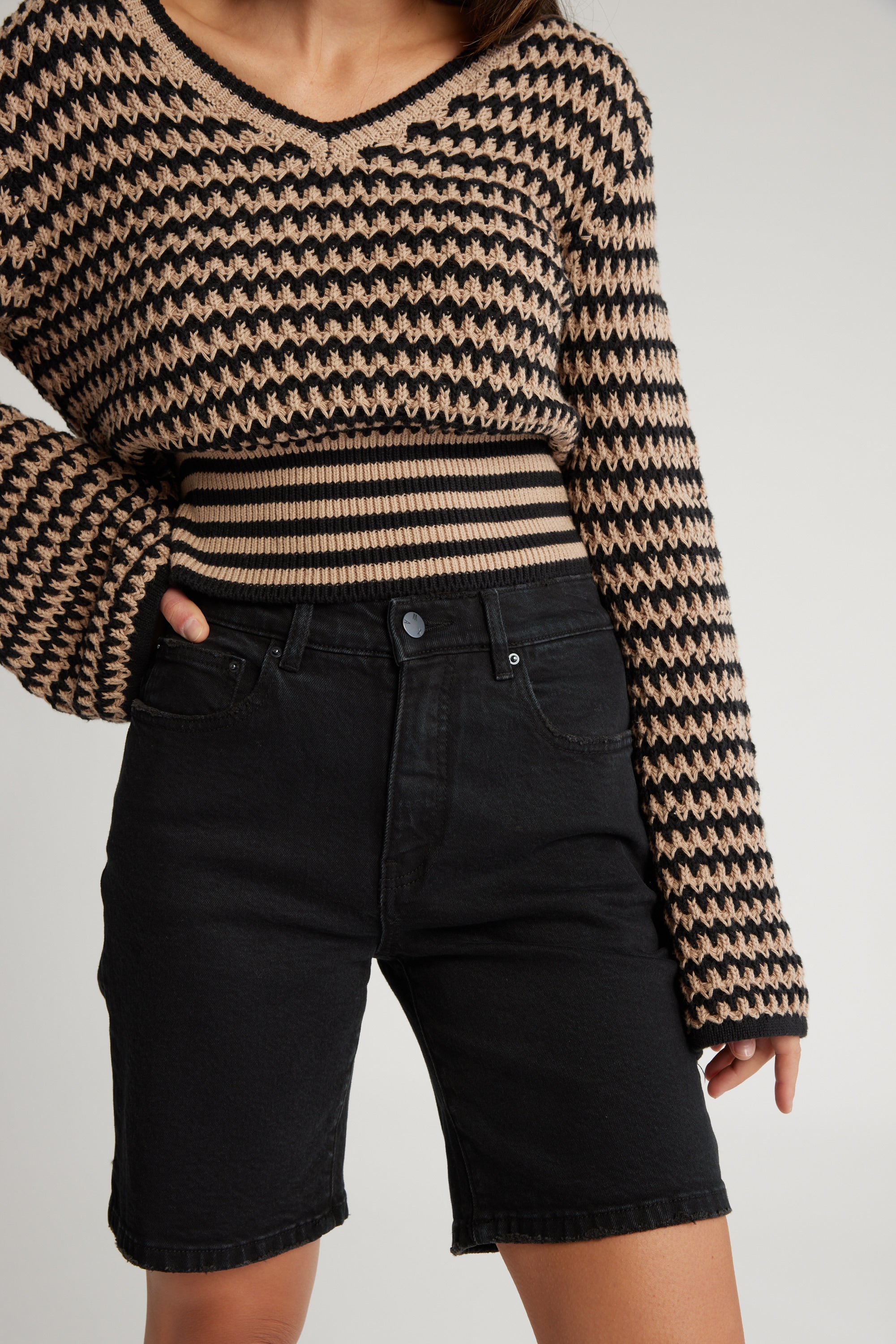 Person wears Max's The Relaxed Straight Denim Short with a black and beige knit sweater, hand on hip.