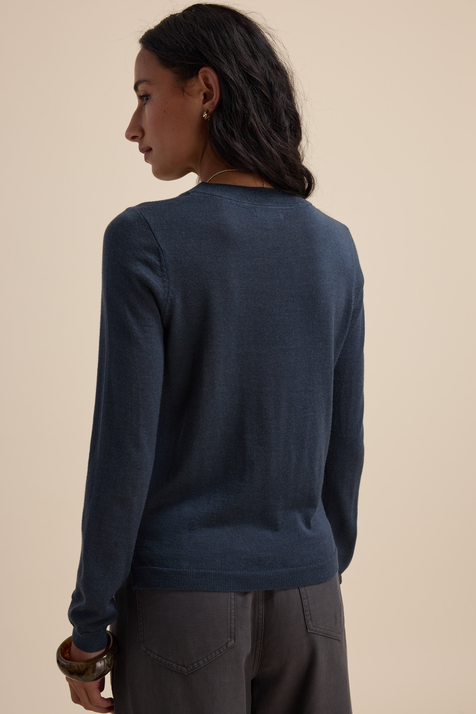 Model in Max’s The Merino Silk Layering Top and gray pants, back view, beige background.