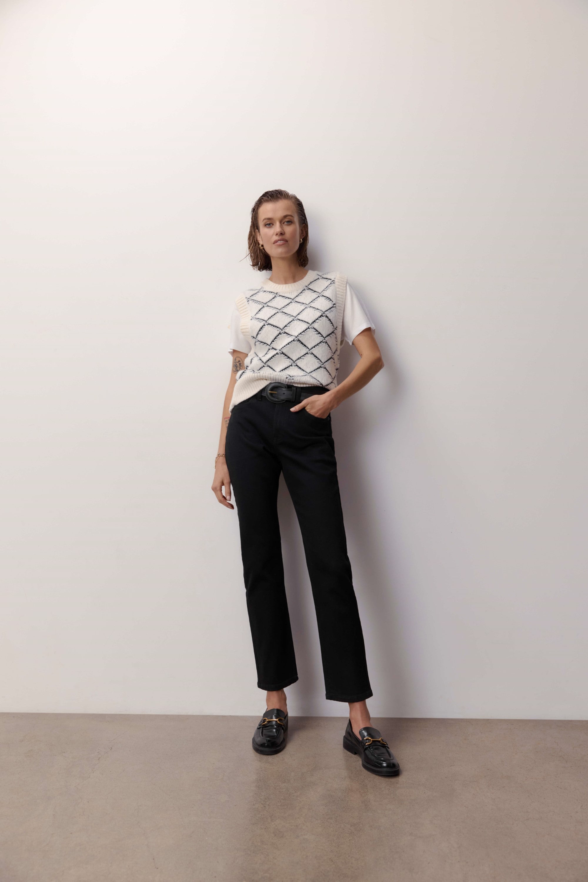 Woman in a white tee and Max Georgia Slim Jeans stands by a white wall.