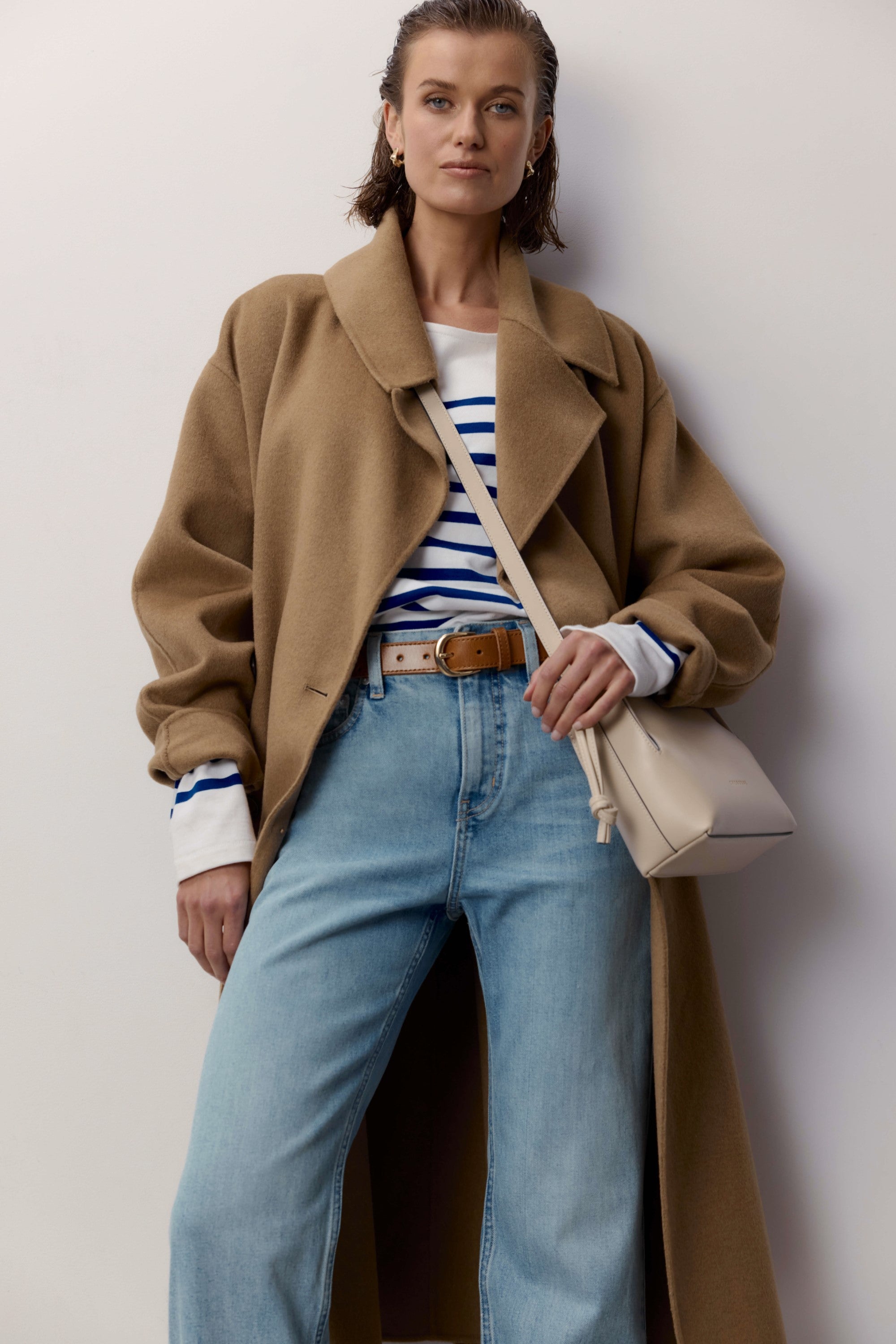 Woman in a camel coat, striped shirt, Max Arizona Straight Jeans, and beige bag.
