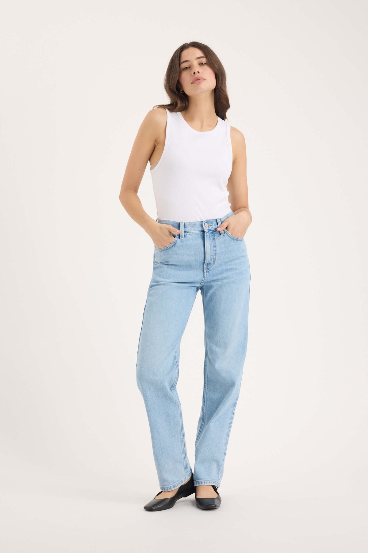 Person in white tank, Max Arizona Straight Jeans, and black flats poses against plain backdrop.