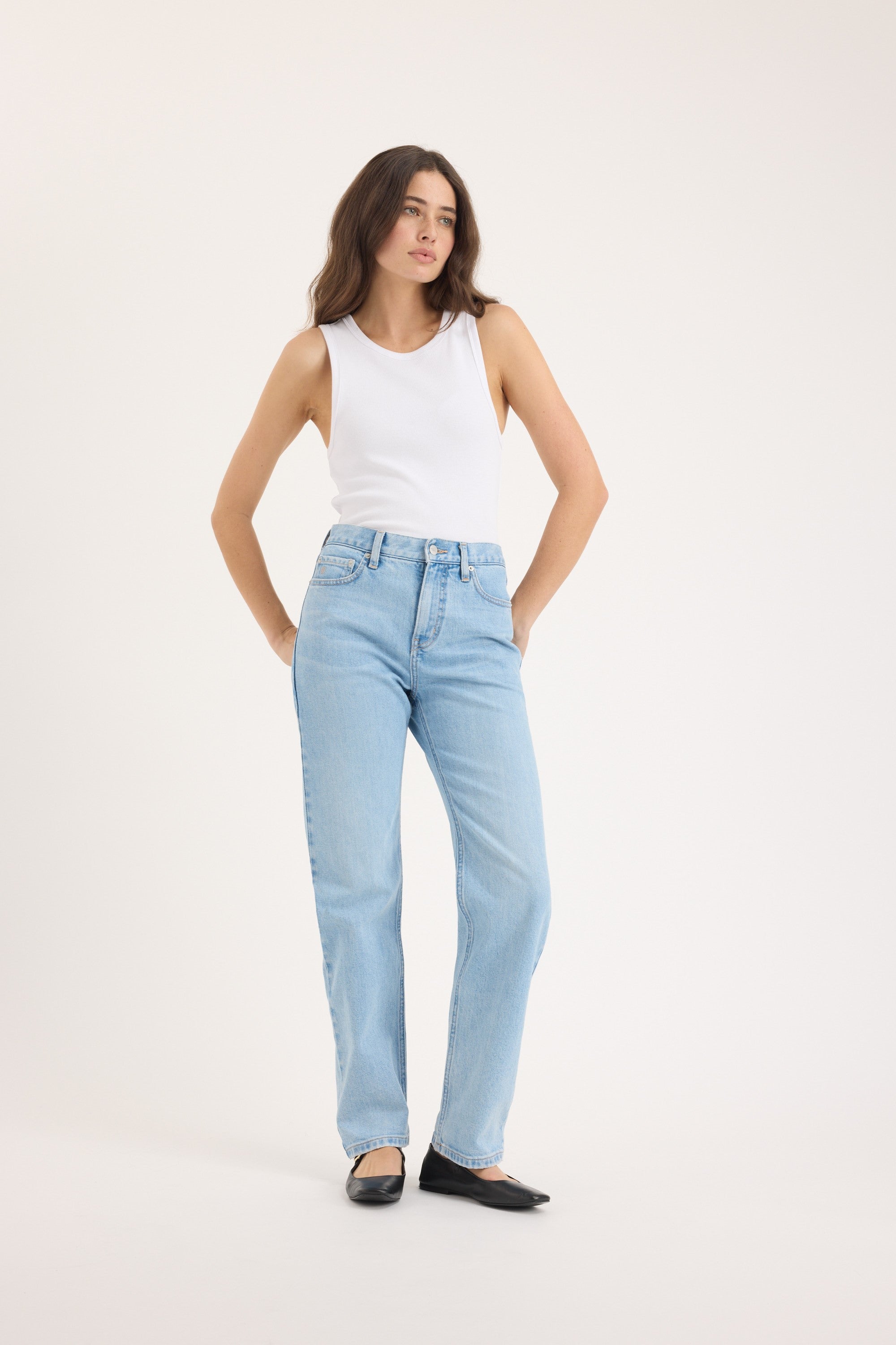 Woman in Arizona Straight Jeans by Max, white tank top, and black flats against a white background.
