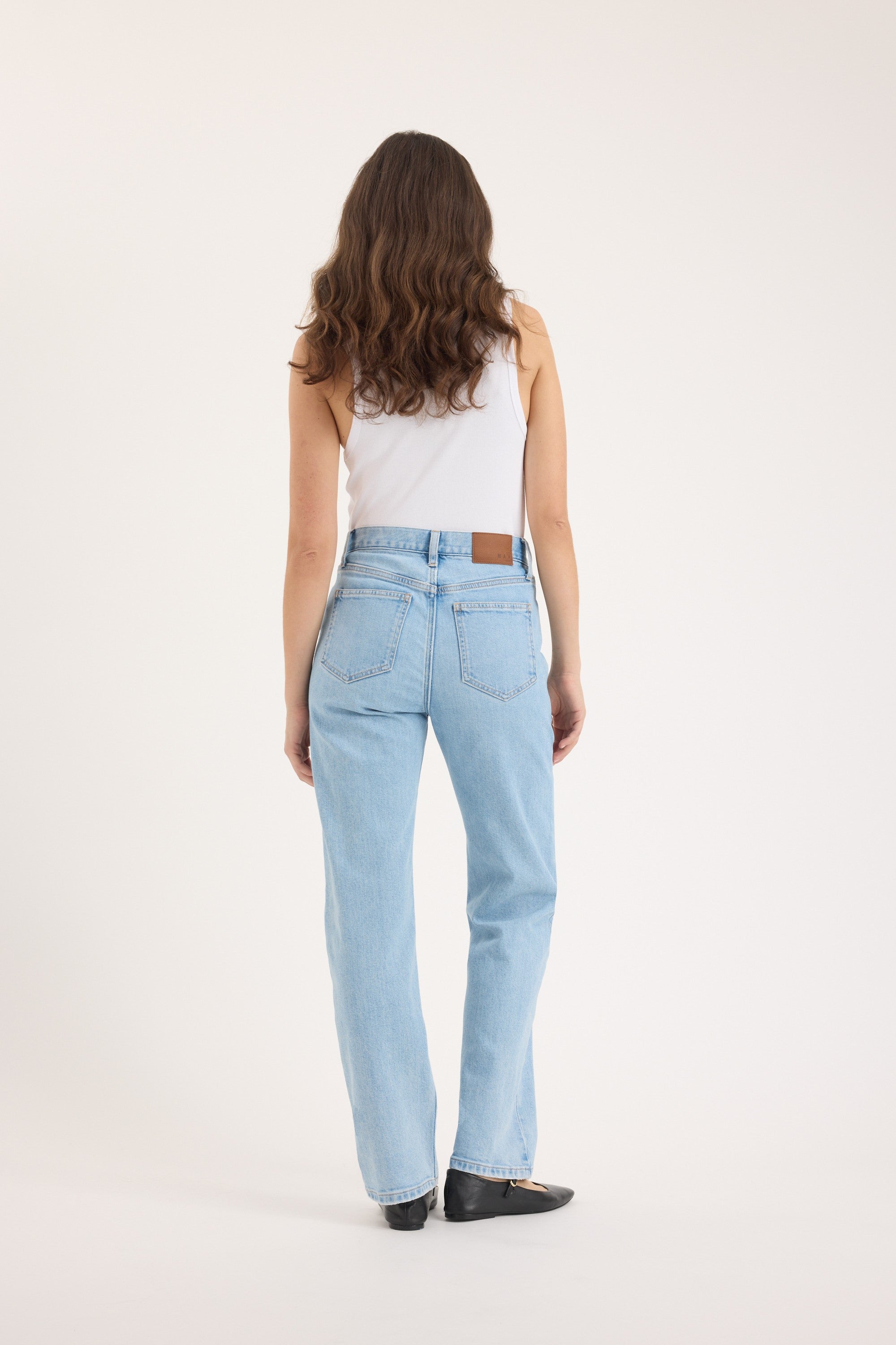 Person in a white tank top and Max Arizona Straight Jeans, standing with back to camera.