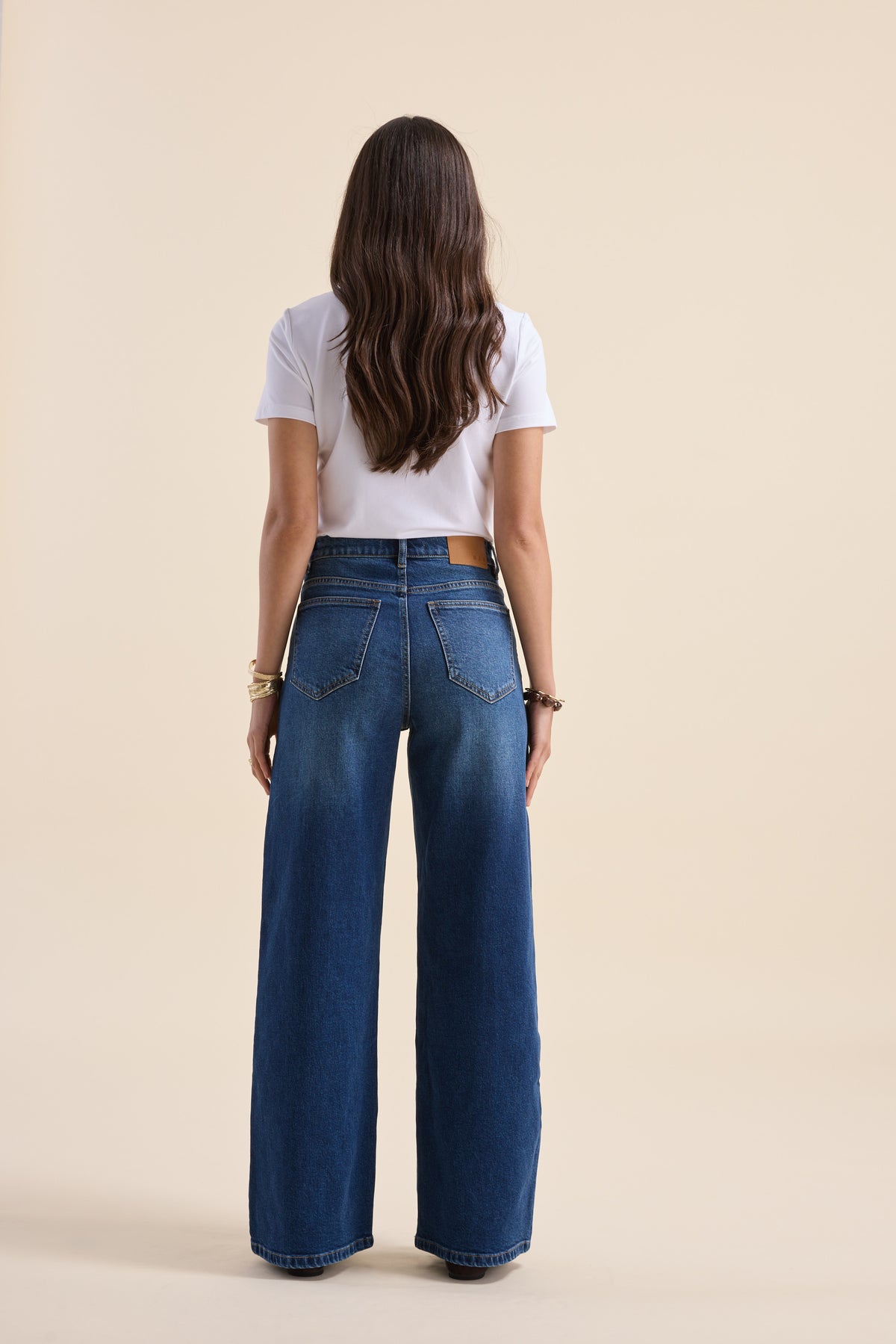 Woman with long hair in white top and Max Nevada Wide jeans, standing facing away.