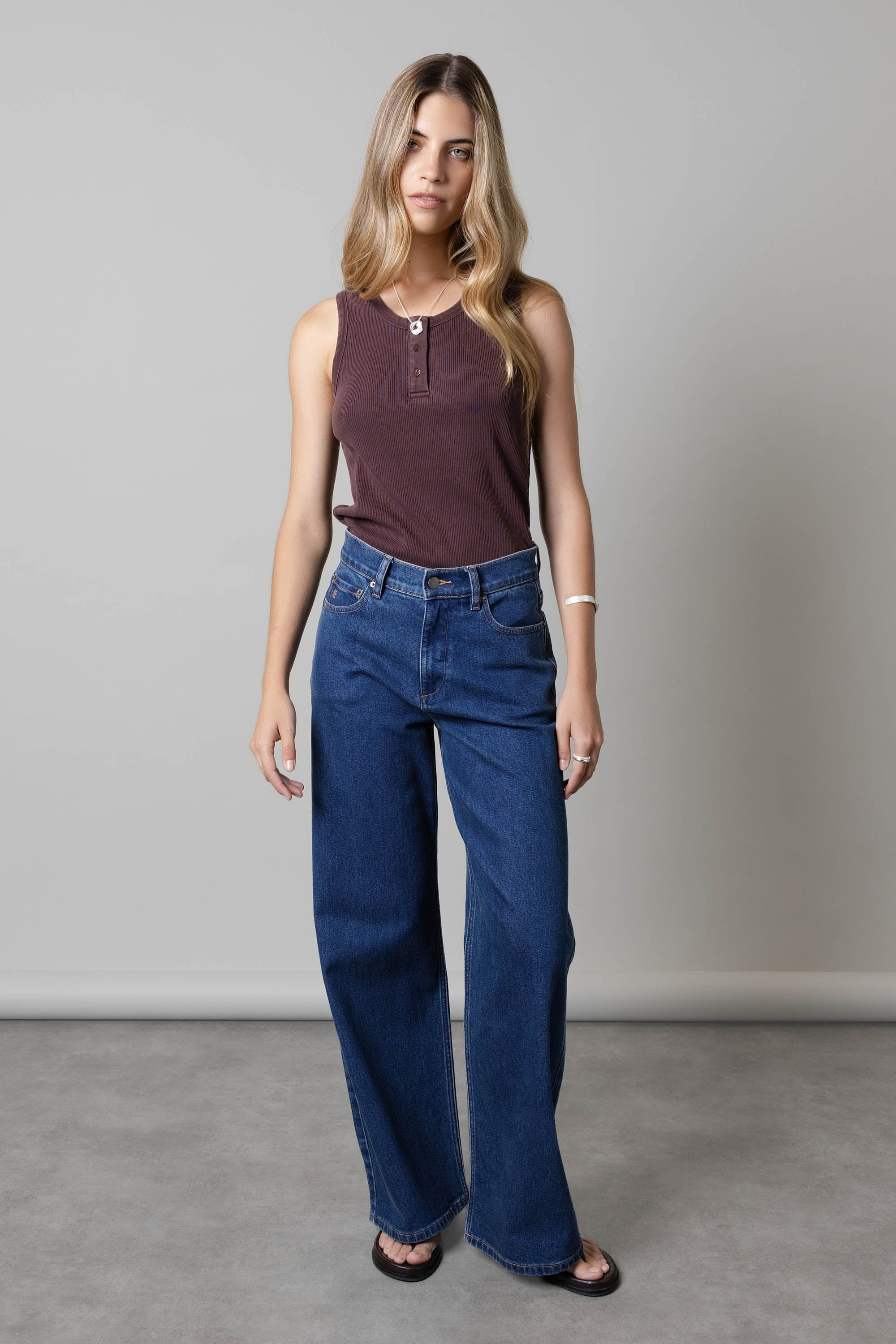 Woman in Nevada Wide Jeans by Max and a brown sleeveless top against a gray background.