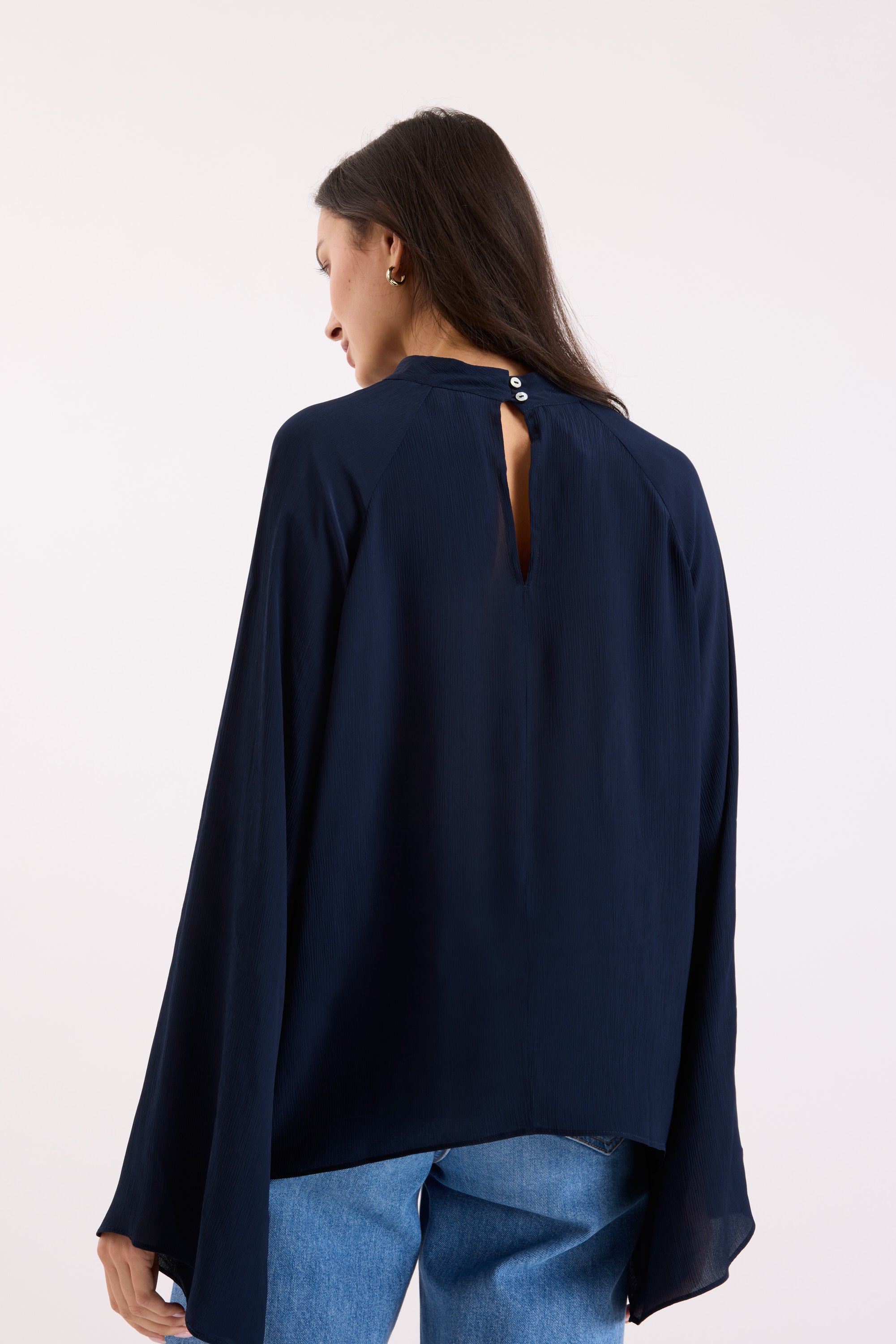 Woman wearing Max Lindsay Textured Blouse in navy with flared sleeves and jeans, back view.