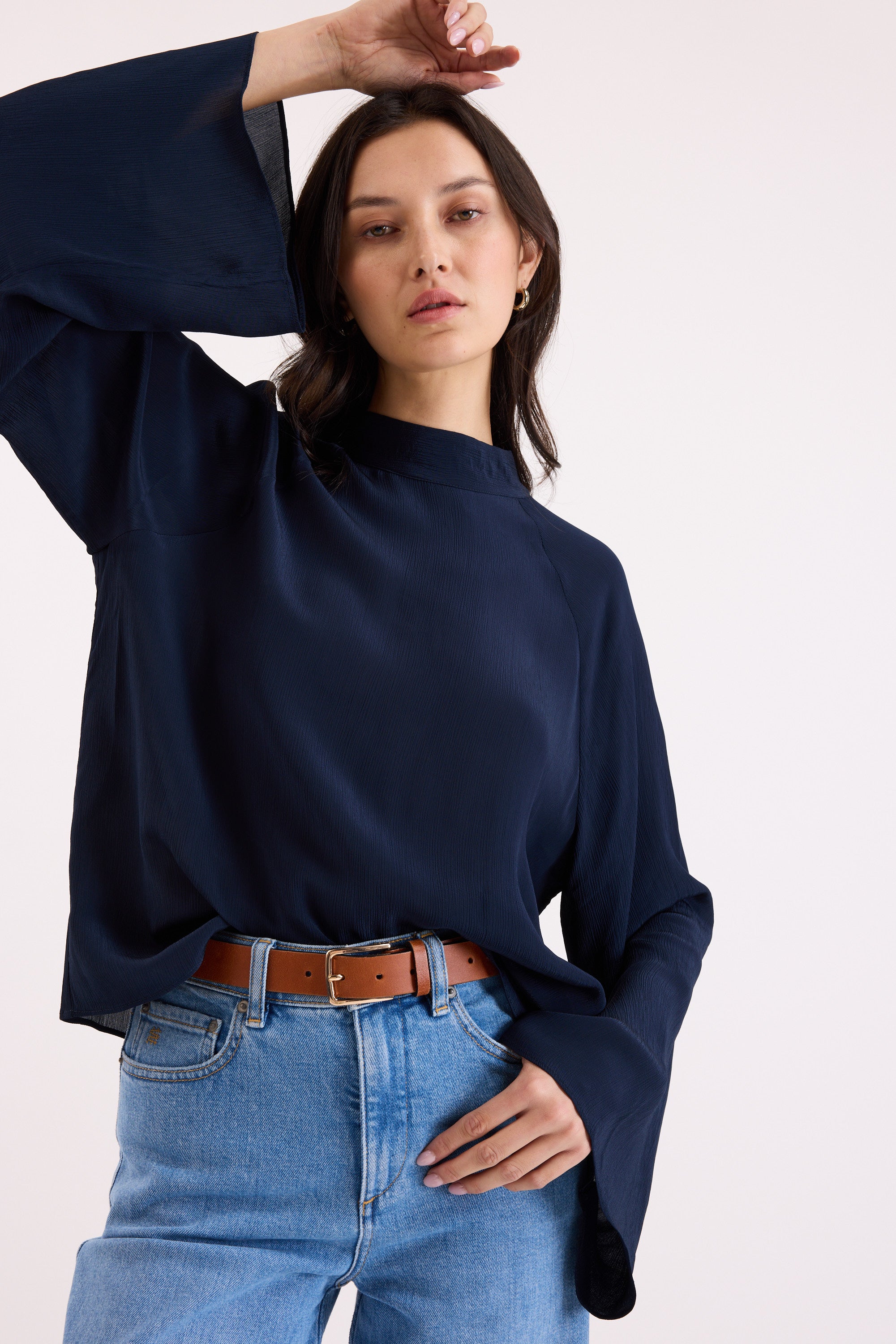 Woman wears Max Lindsay Textured Blouse in navy with flared sleeves and blue jeans, hand raised.