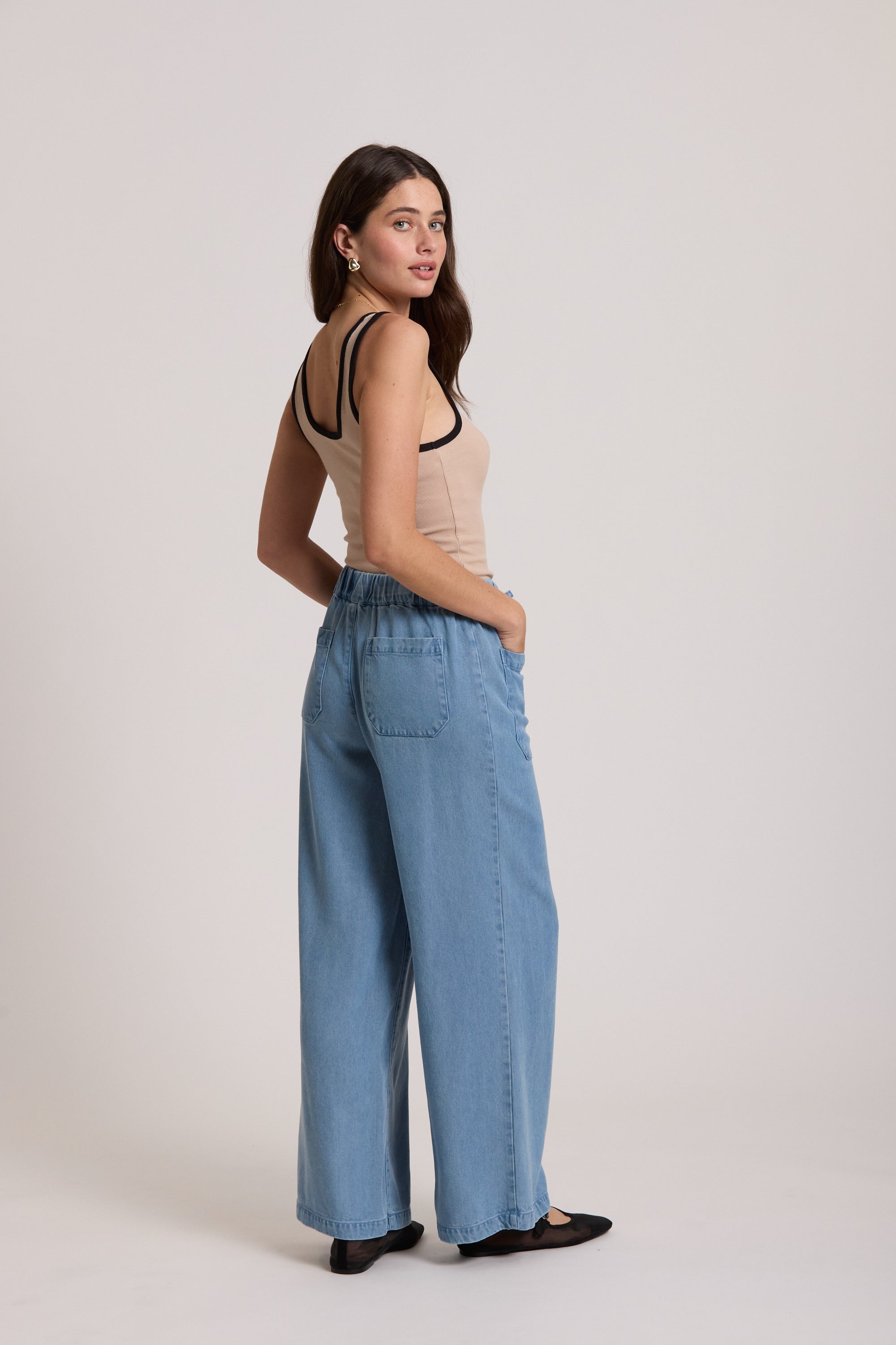 Woman in The Contrast Trim Tank by Max and wide-leg jeans stands sideways, facing the camera.