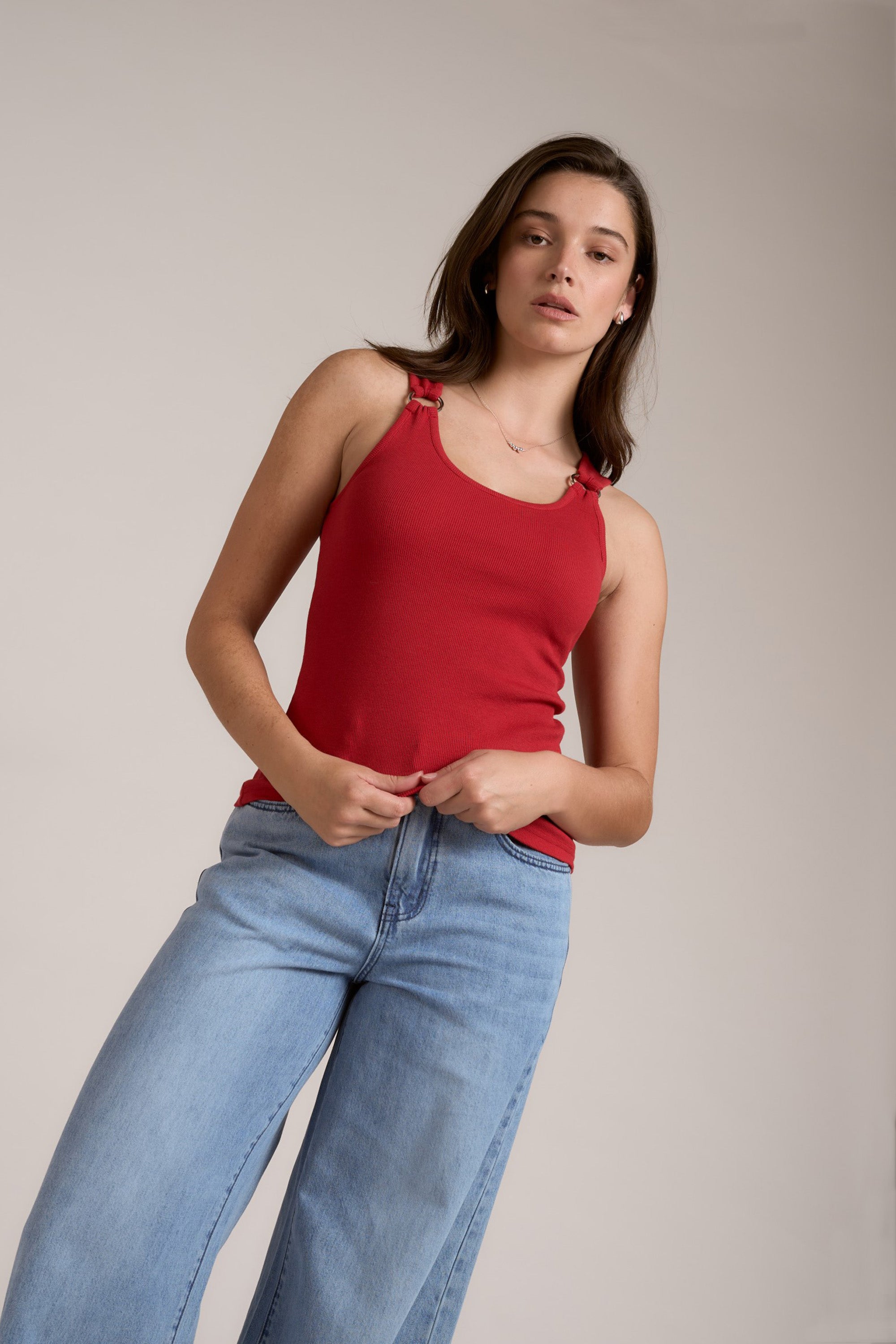 Woman wears Max's Eliza Ring Detail Tank in red with blue jeans against a plain light background.