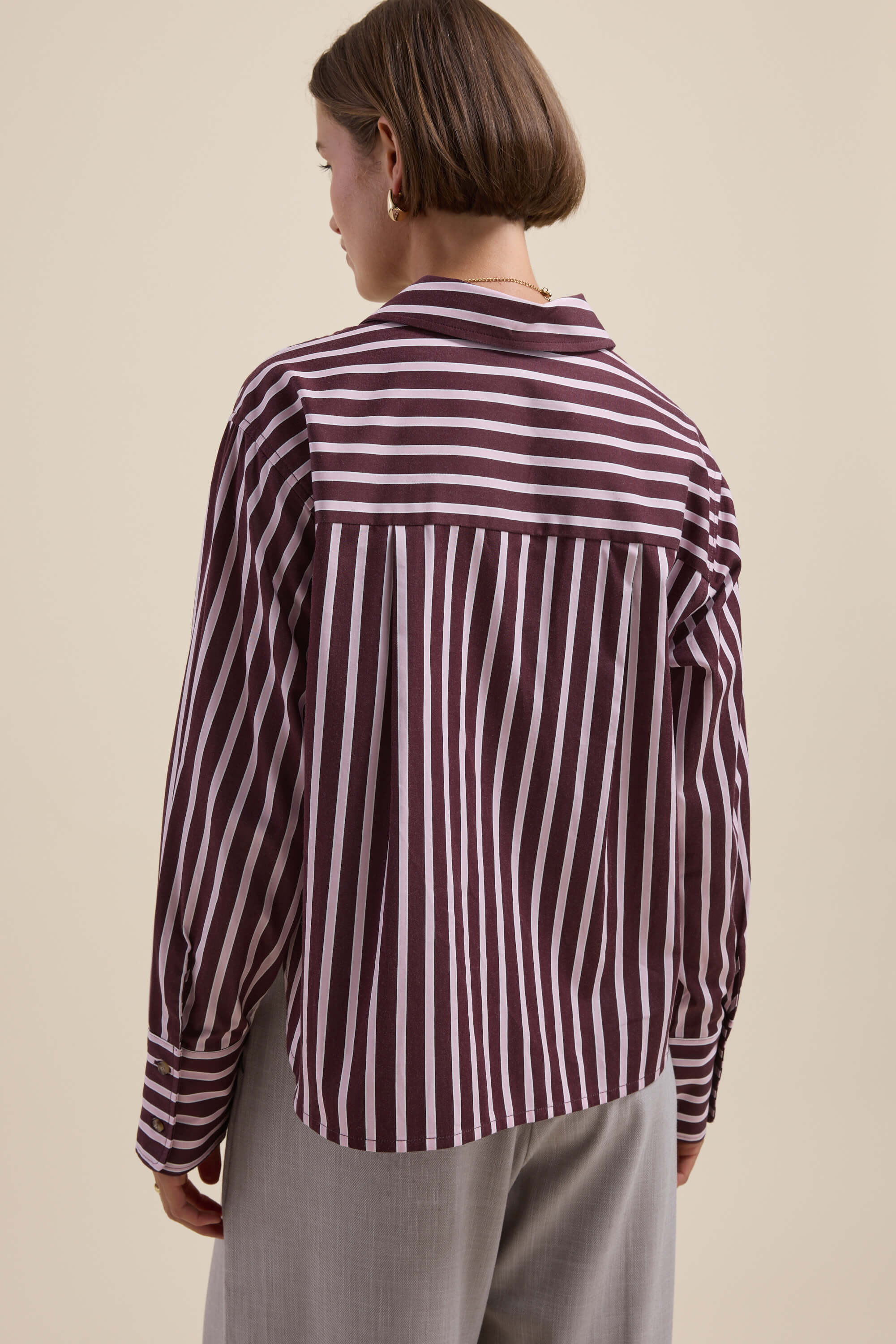 Woman in Max's Leah Stripe Detail Shirt, maroon/white stripes, with light grey pants.