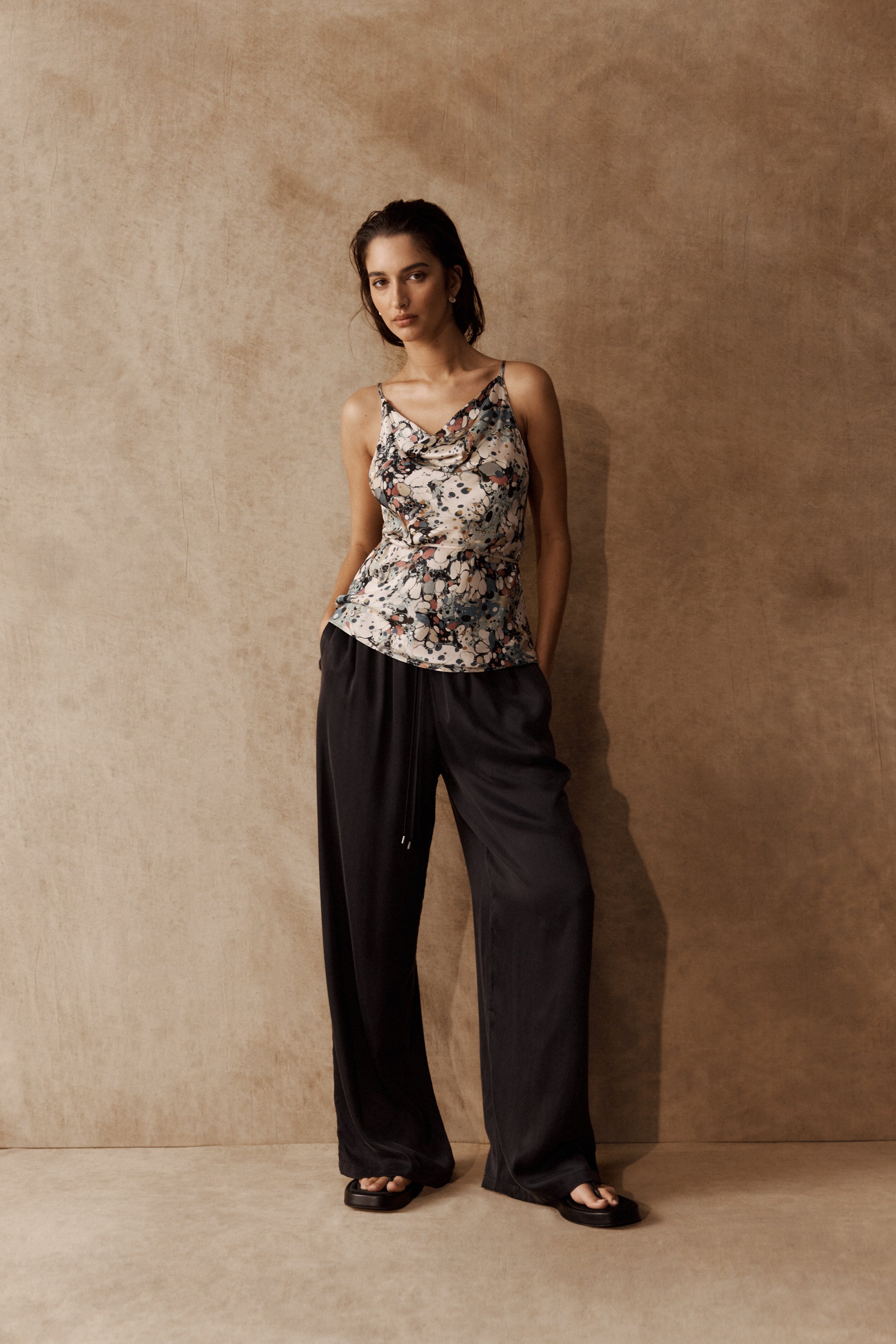 Woman in Max Lola Cowl Neck Top and wide-leg black pants stands against a beige background.