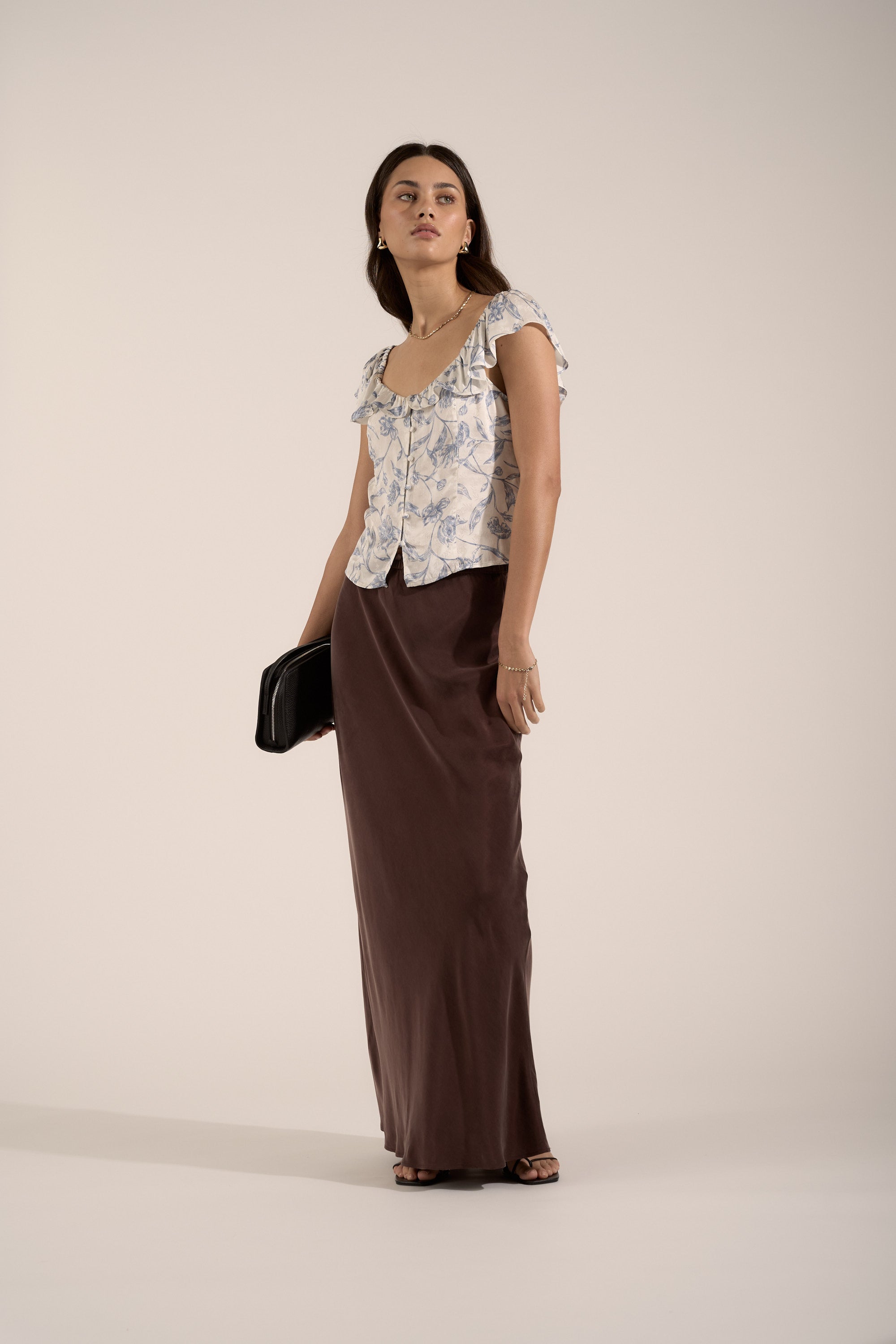 Woman in a Max Ingrid Frill Detail Blouse and brown skirt holds a black clutch.