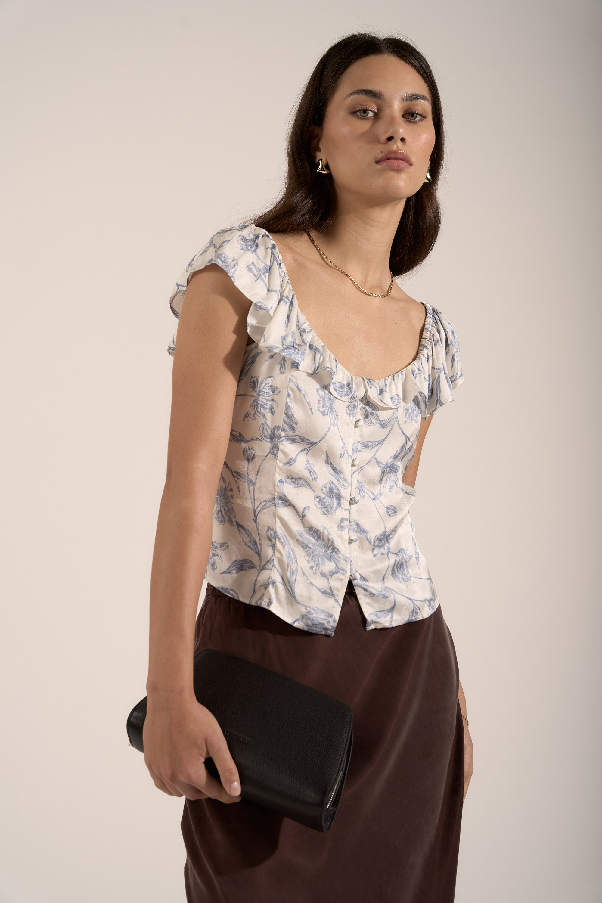 Woman wears Max Ingrid Frill Detail Blouse with brown skirt and holds black clutch.