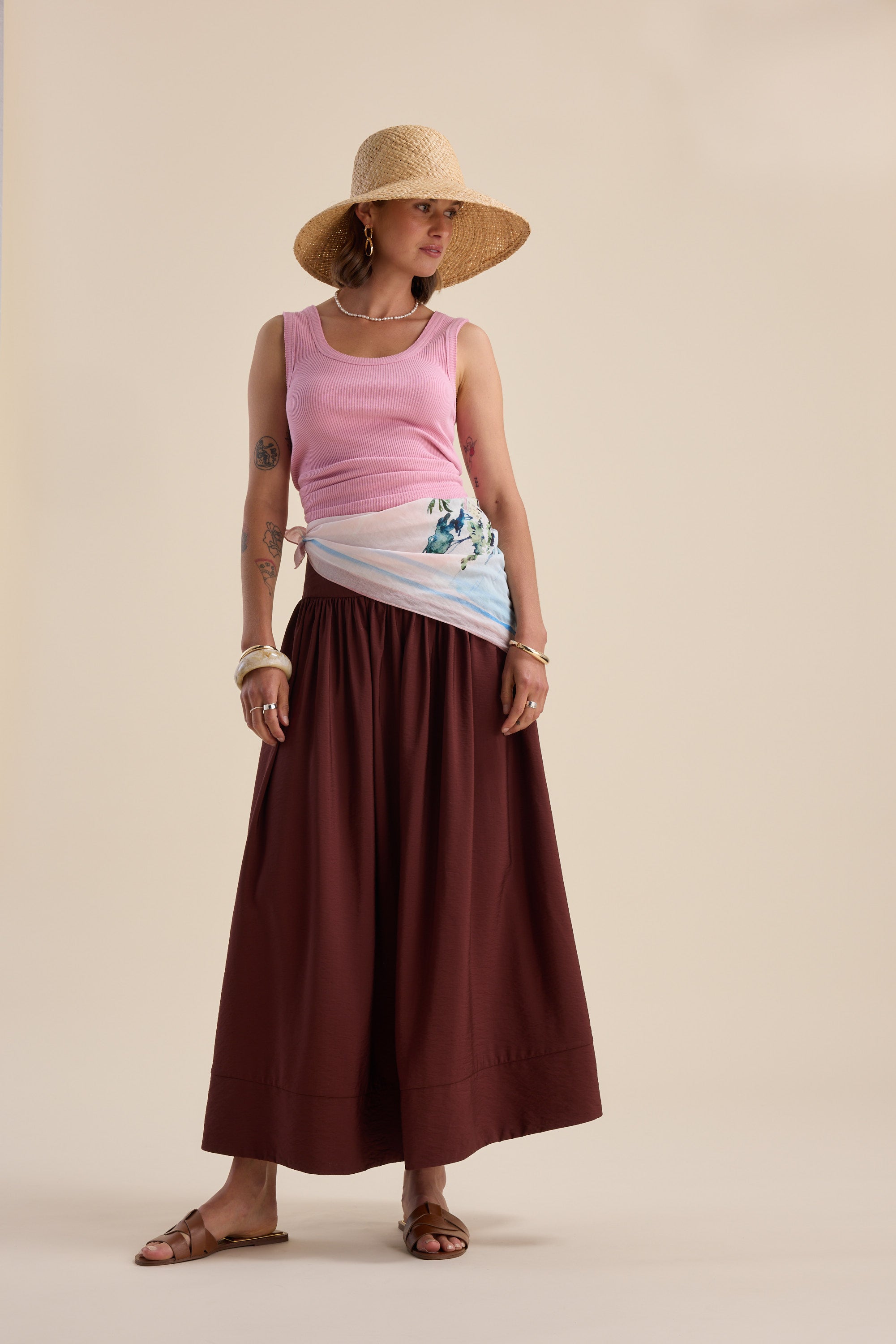 Woman in a straw hat, pink top, Max Carrie Tiered Skirt, and sandals, standing sideways.