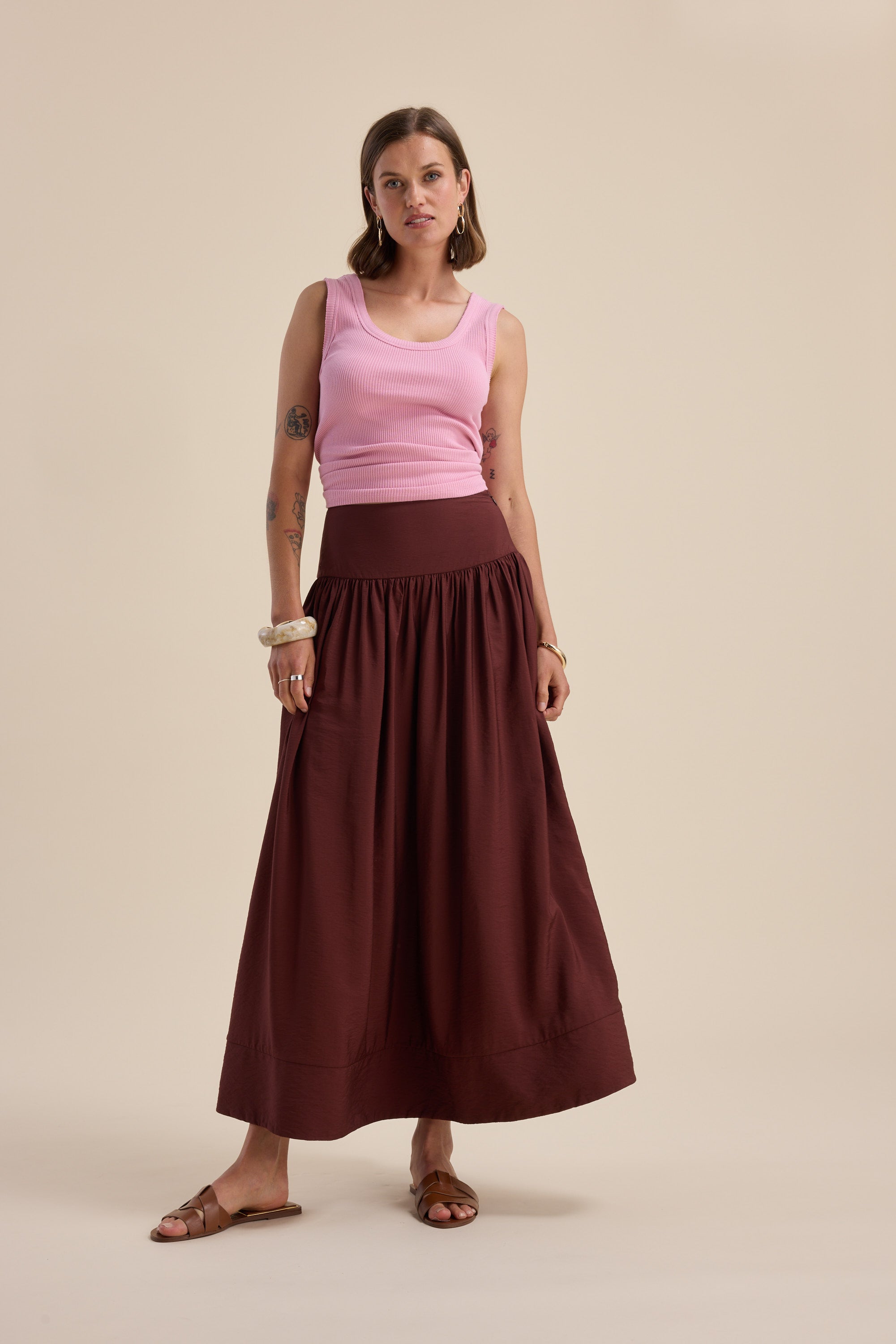 Woman in Max Carrie Tiered Skirt, pink tank top, and sandals against a beige background.