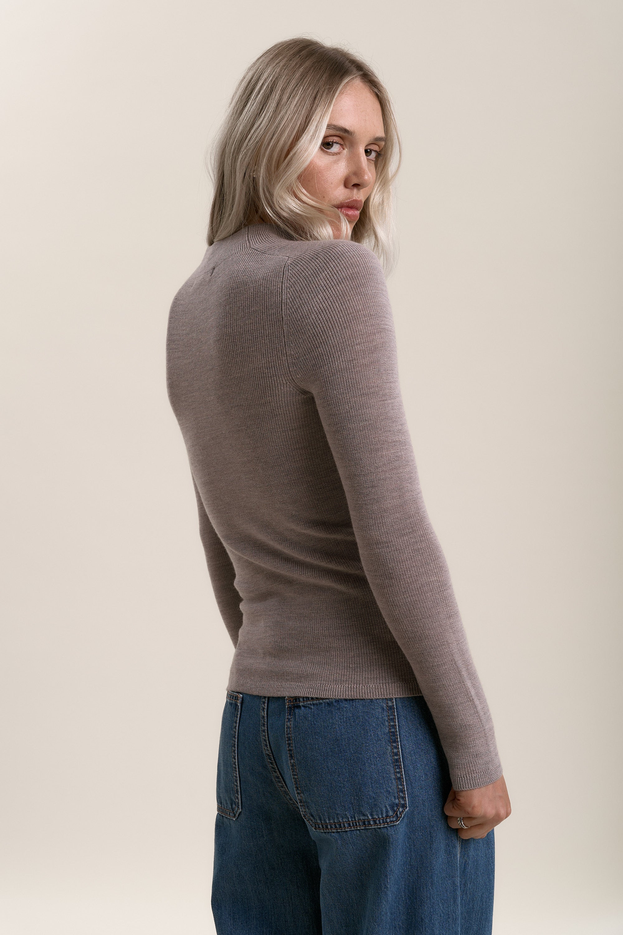 Blonde woman in Max Alexis Merino Long Sleeve and jeans, looking over her shoulder.