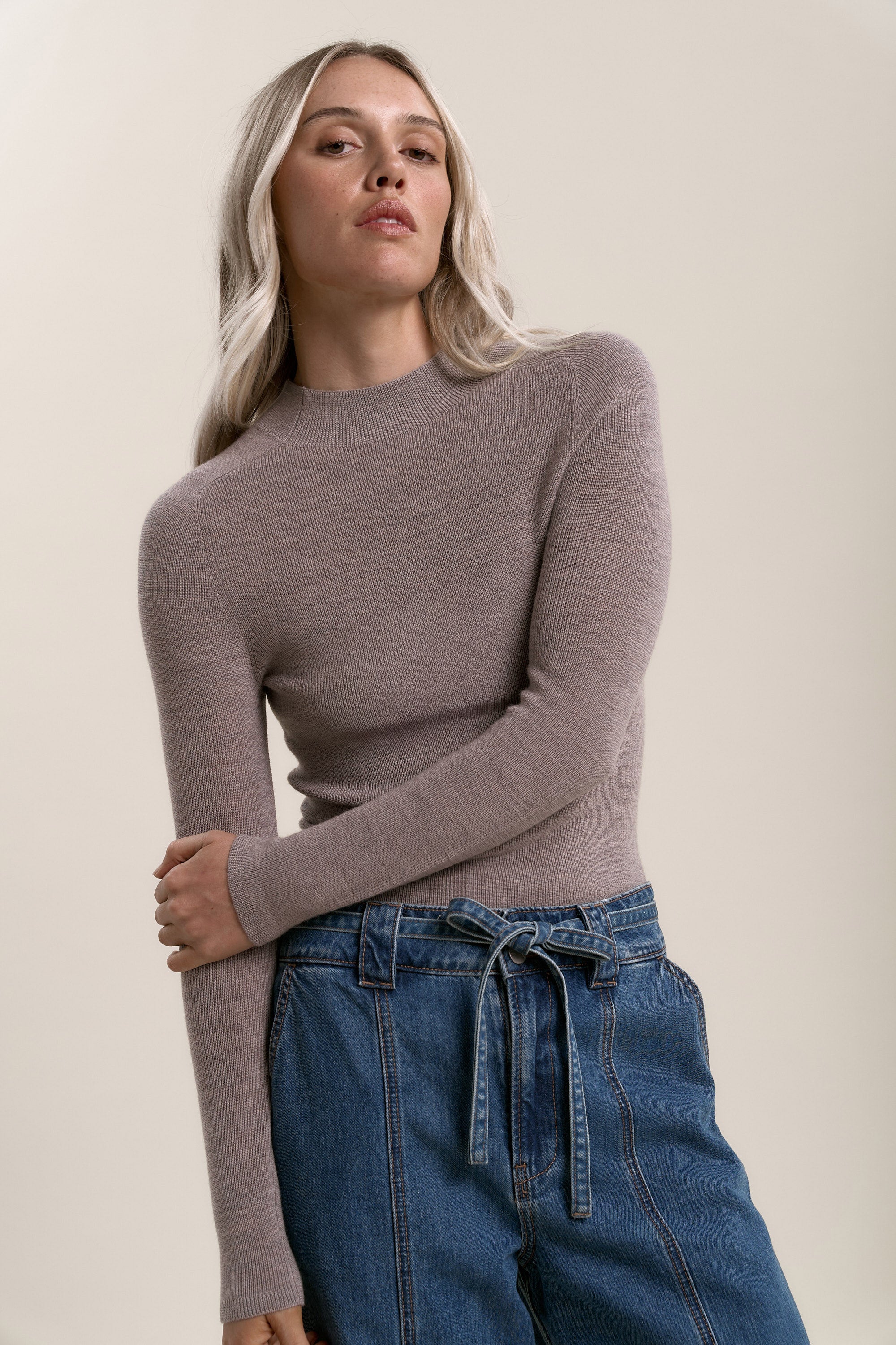 Woman wears the Max Alexis Merino Long Sleeve in beige and high-waisted blue jeans, arms crossed.