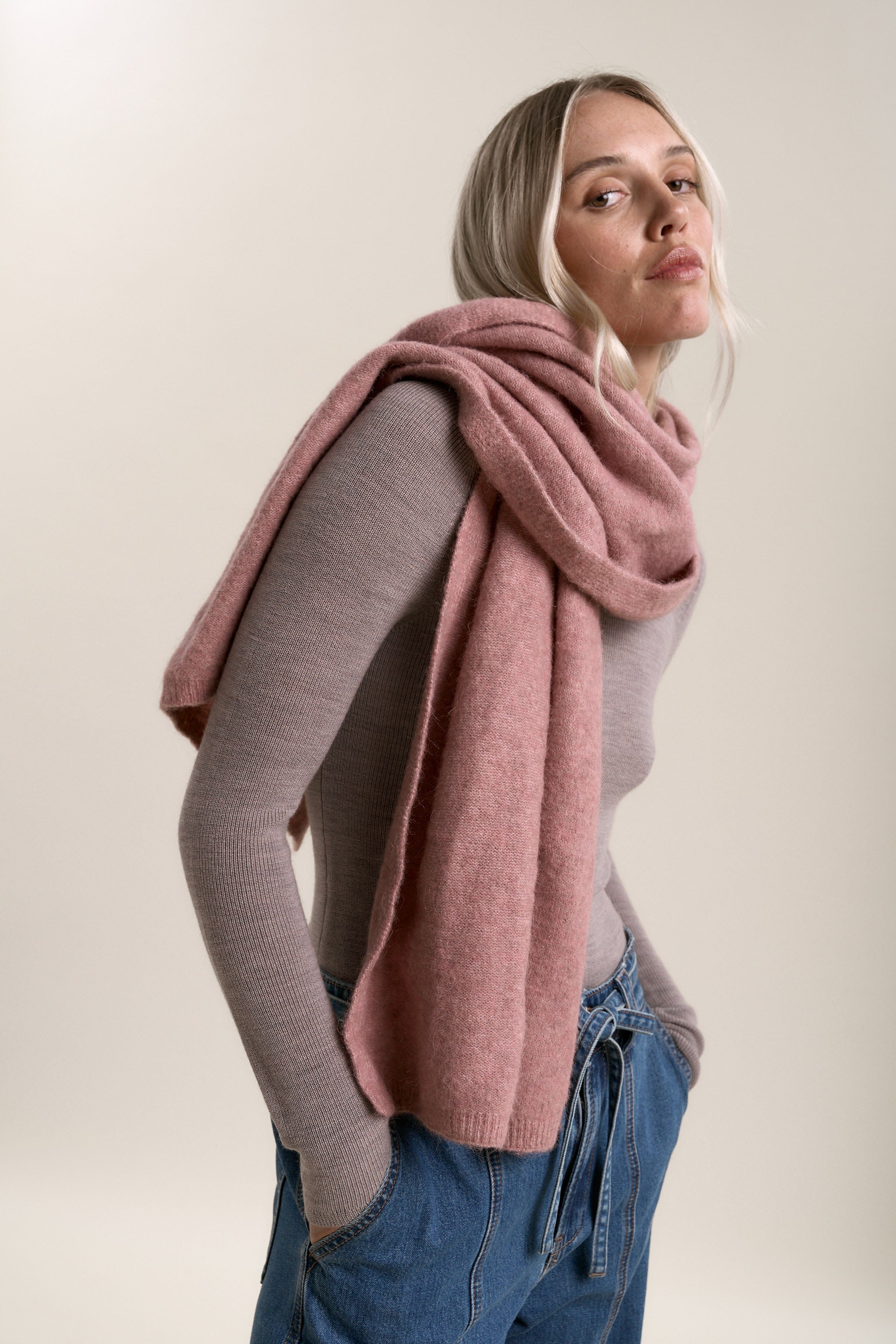 Woman in Alexis Merino Long Sleeve by Max, pink scarf, and blue jeans with hands in pockets.