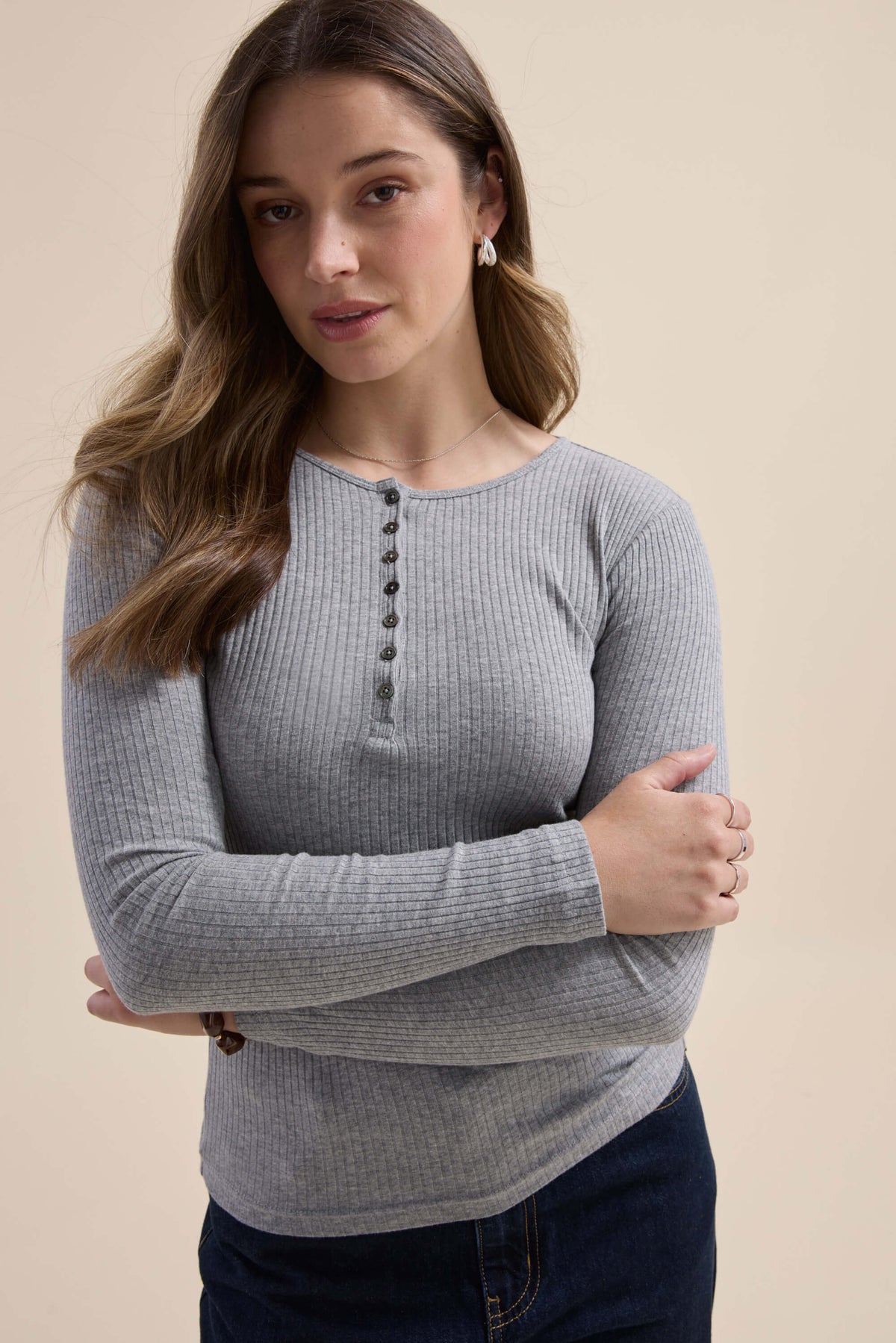 Woman wears Elementary Ribbed Henley, arms crossed, against beige background.