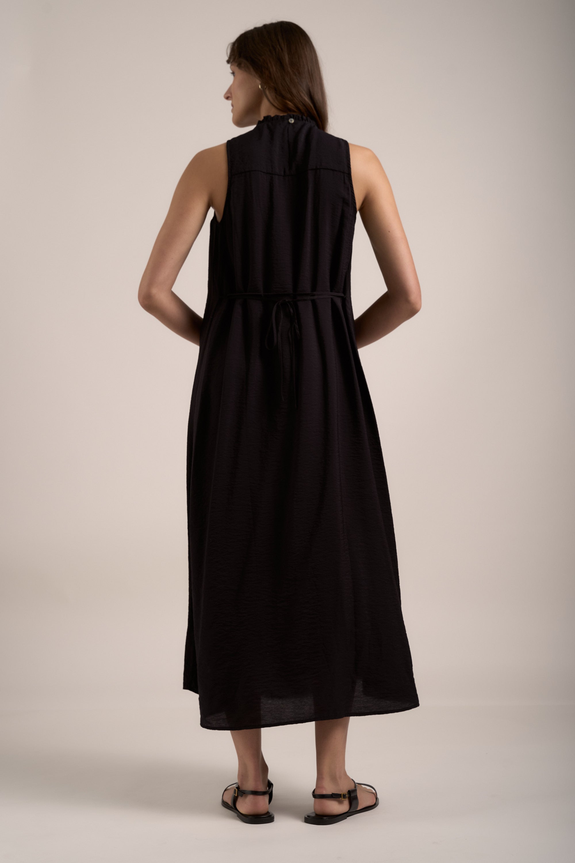 Woman in a Max Sherry Smock Detail Dress, sleeveless and black, stands with her back to camera.