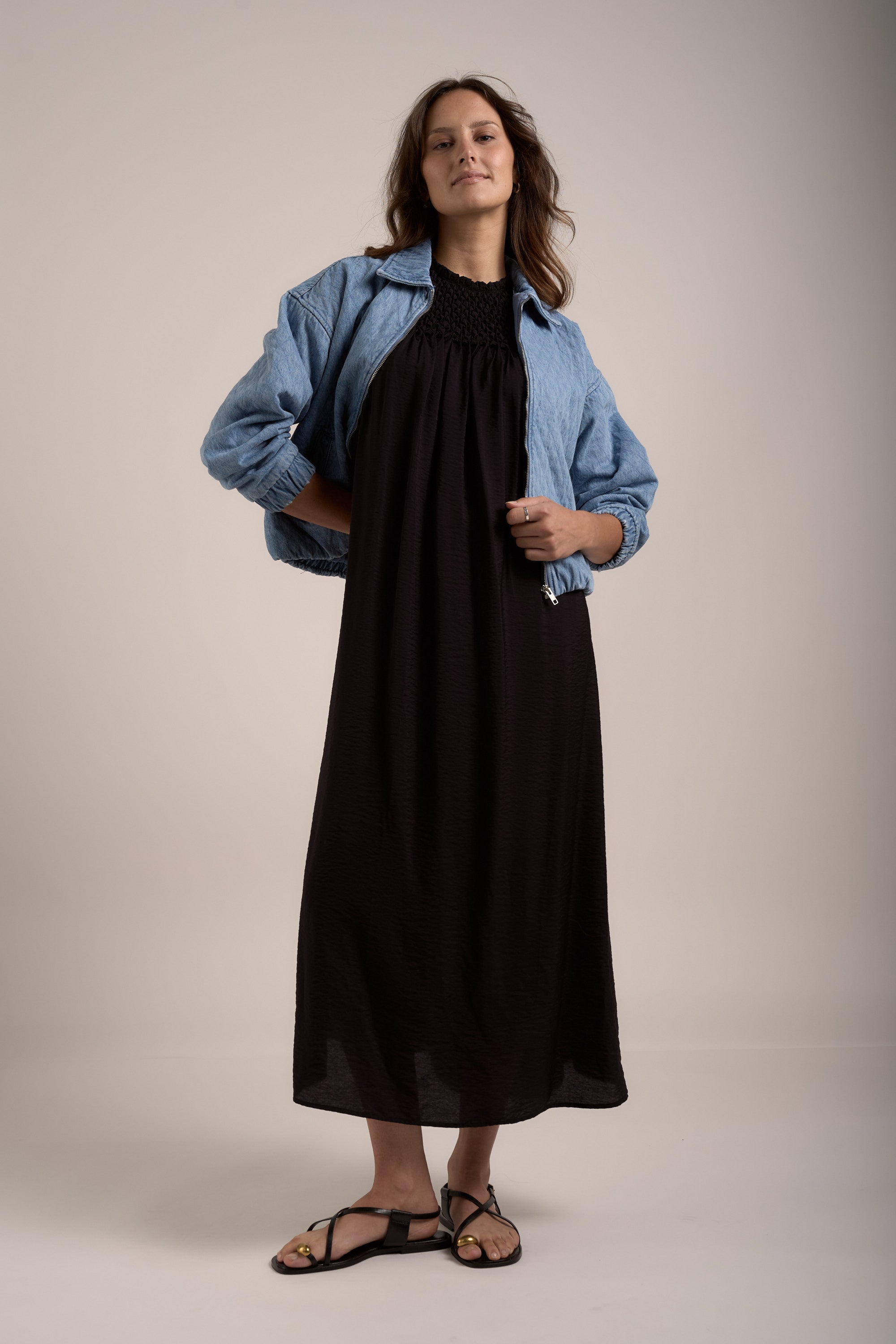 Woman in Sherry Smock Detail Dress by Max, denim jacket, and sandals against plain background.