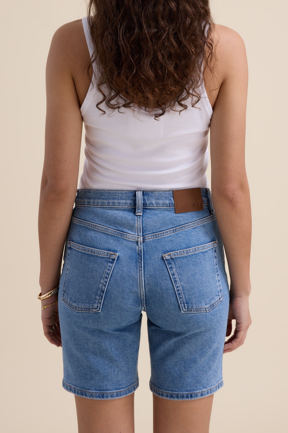 A woman in Max's The Classic Denim Short and a white tank top, seen from the back.