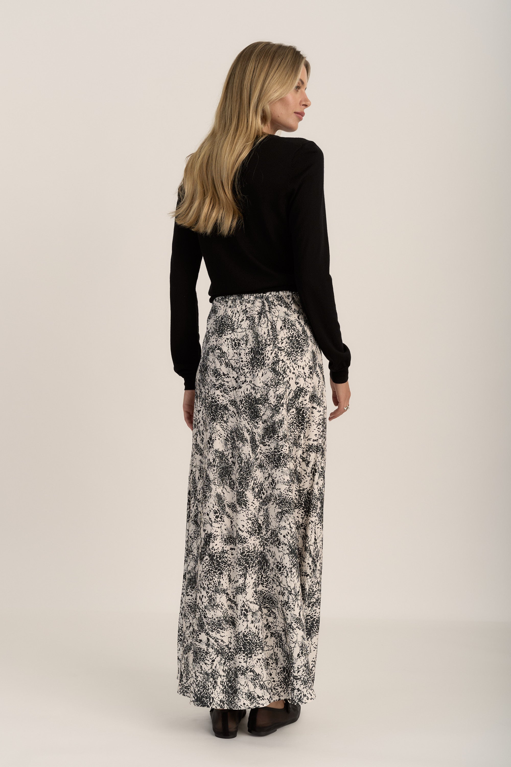 Woman in a black top, Max Henry Maxi Slip Skirt, and black shoes, facing away.